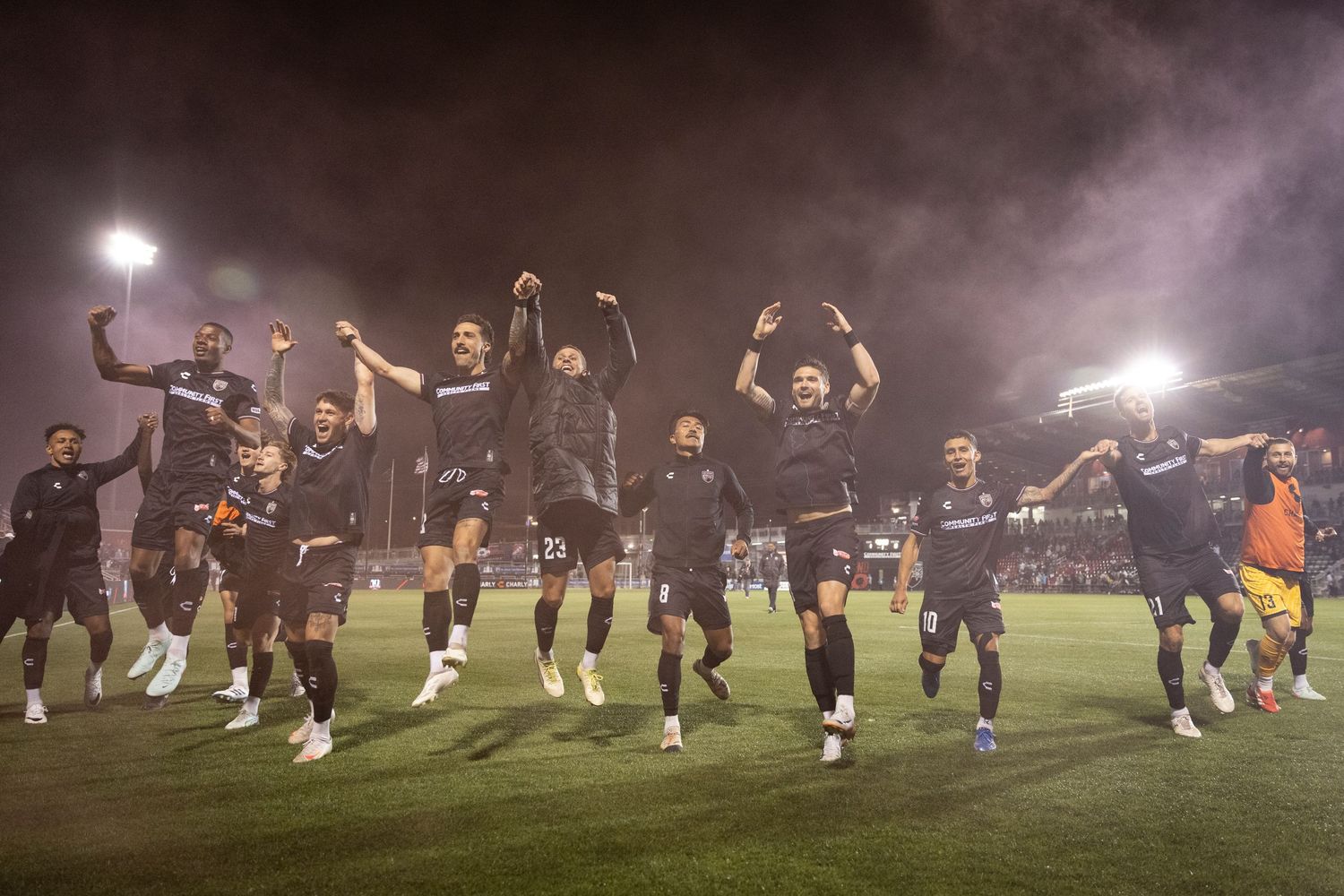 Soccer team celebrates with fans after victory in smoky stadium atmosphere.