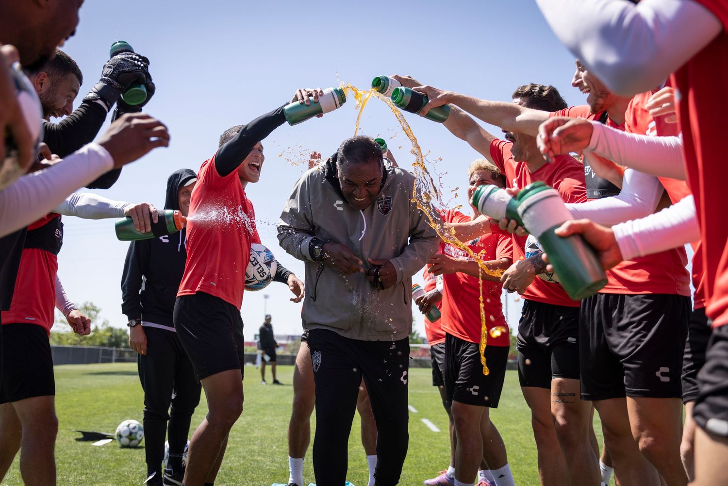 Soccer team celebrates with a water bottle arch on the field during a sunny day celebration.
