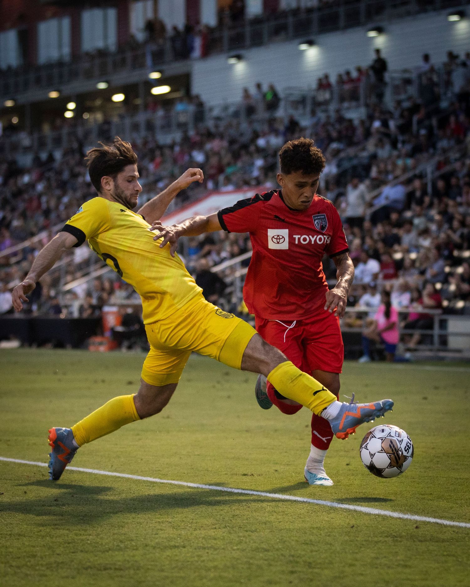 Soccer players in yellow and red jerseys battle for ball possession during match.