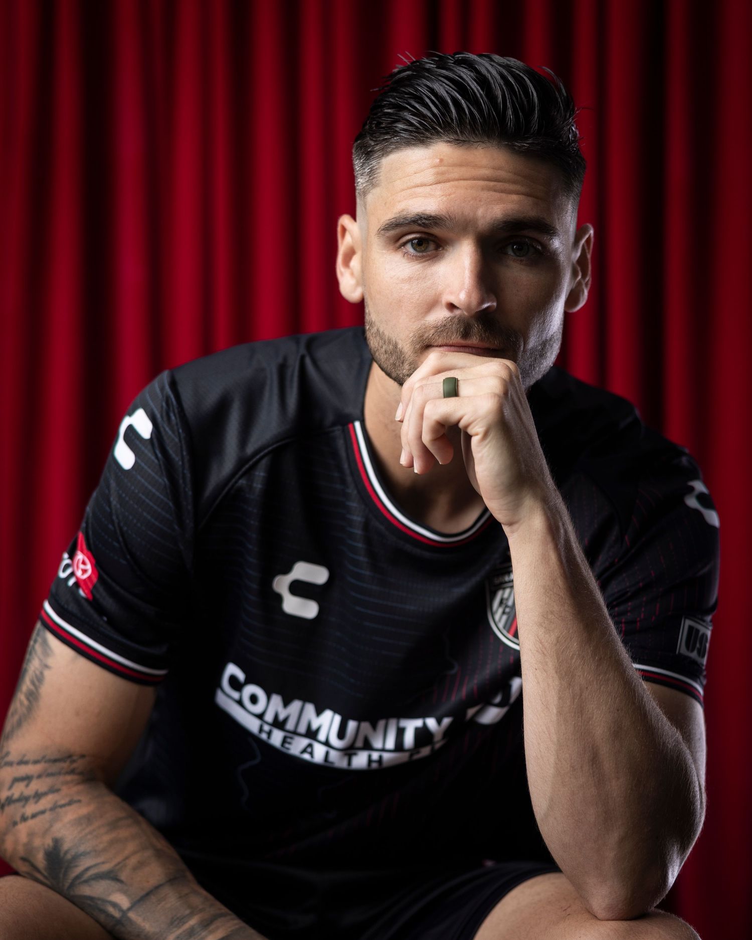 Professional athlete in black uniform poses thoughtfully against red curtain backdrop.