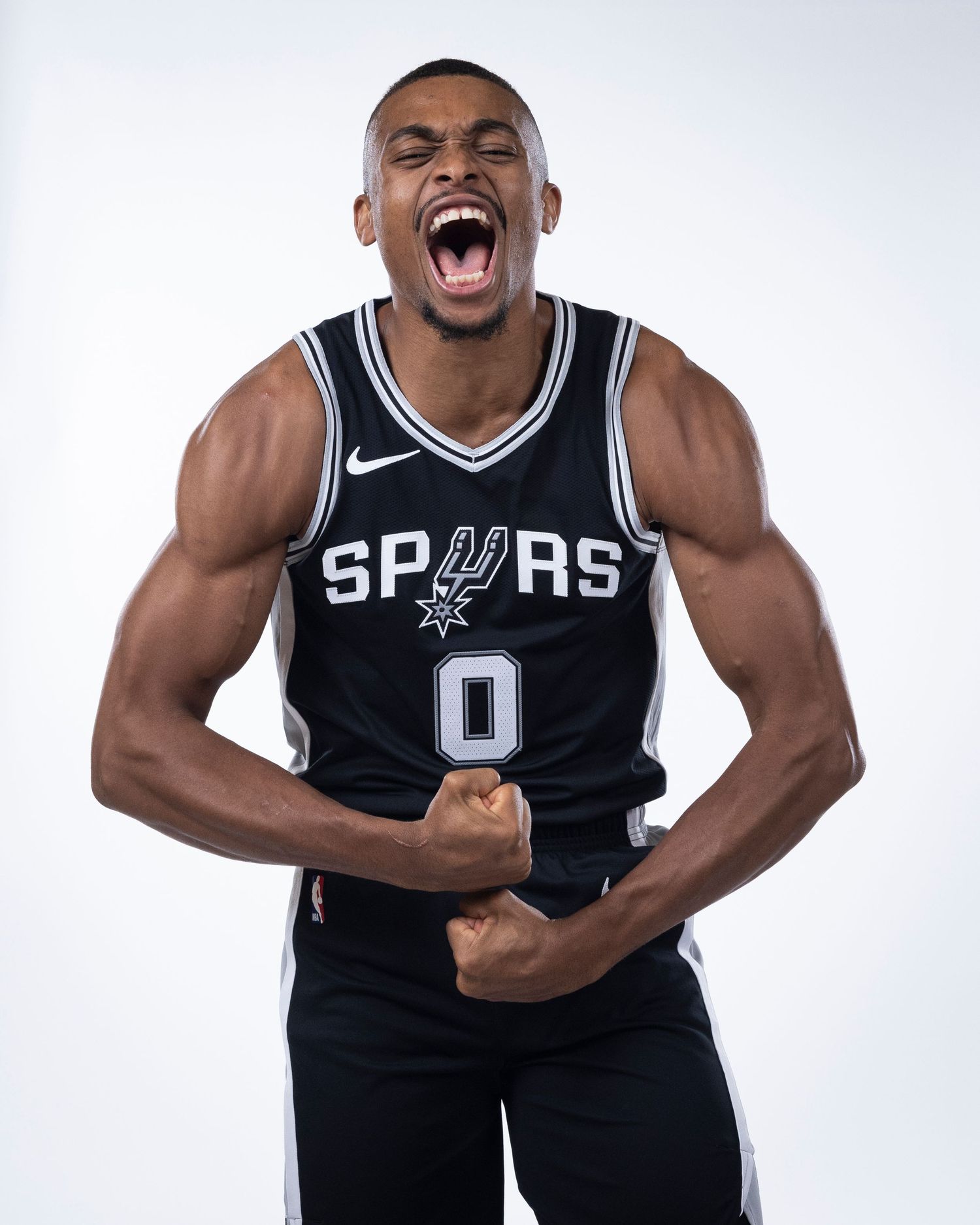 San Antonio Spurs player wearing number 0 jersey flexes muscles and shouts with intense emotion during photo shoot.