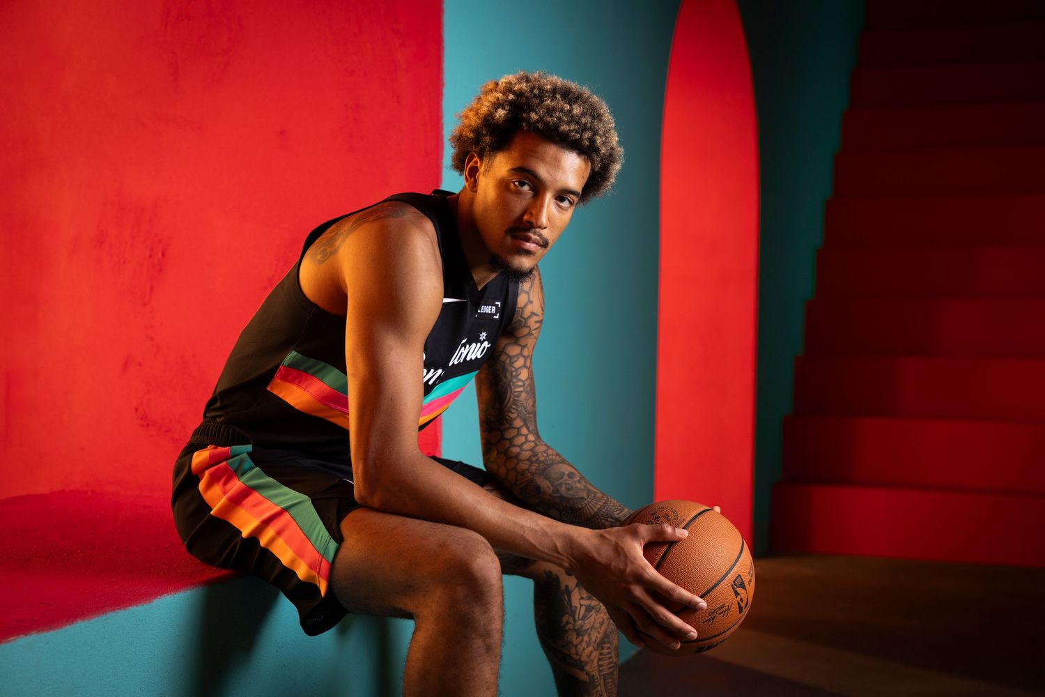 Tattooed NBA player poses with basketball in San Antonio Spurs black City Edition jersey.