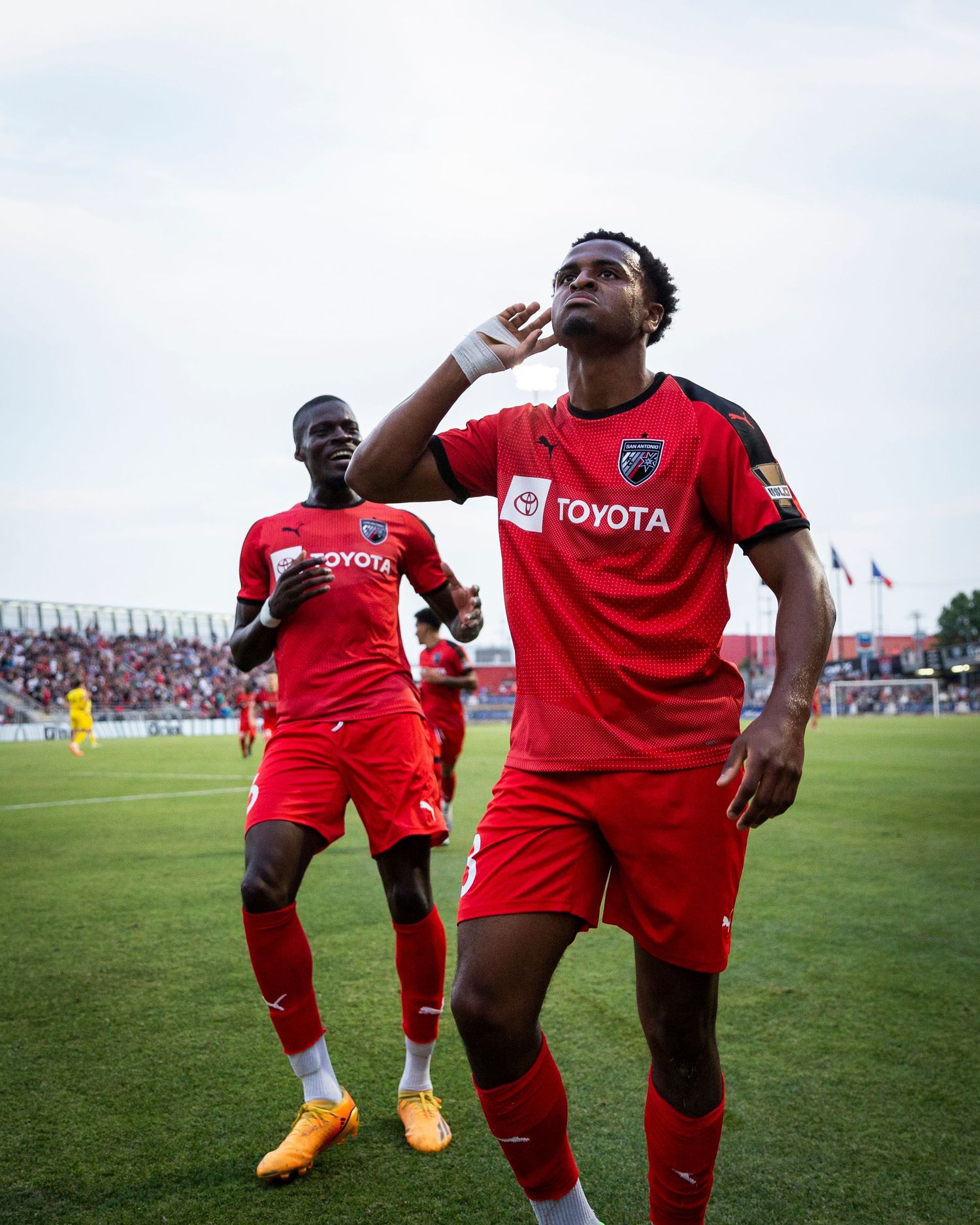 Soccer players in red Toyota jerseys celebrate with synchronized dance moves on the field during a match.