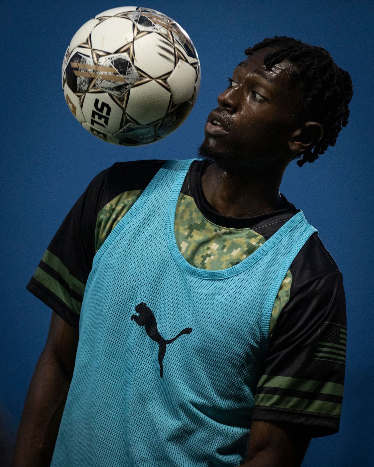 Soccer player in light blue training vest practices ball control against blue background.