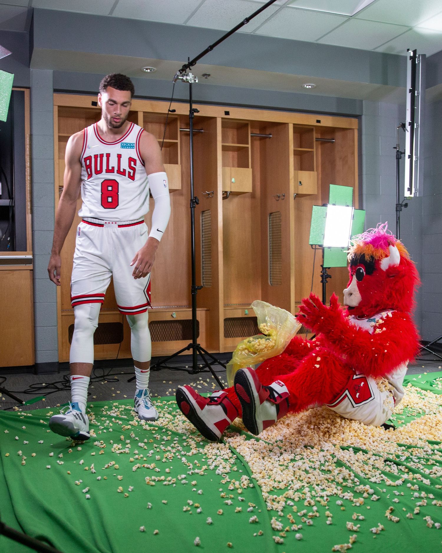 Bulls player posing with team mascot Benny the Bull surrounded by popcorn in locker room.