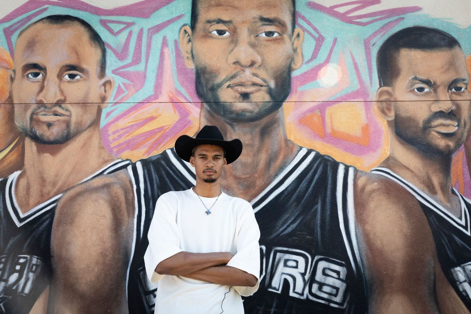 Person in black hat stands in front of large basketball mural with colorful background.