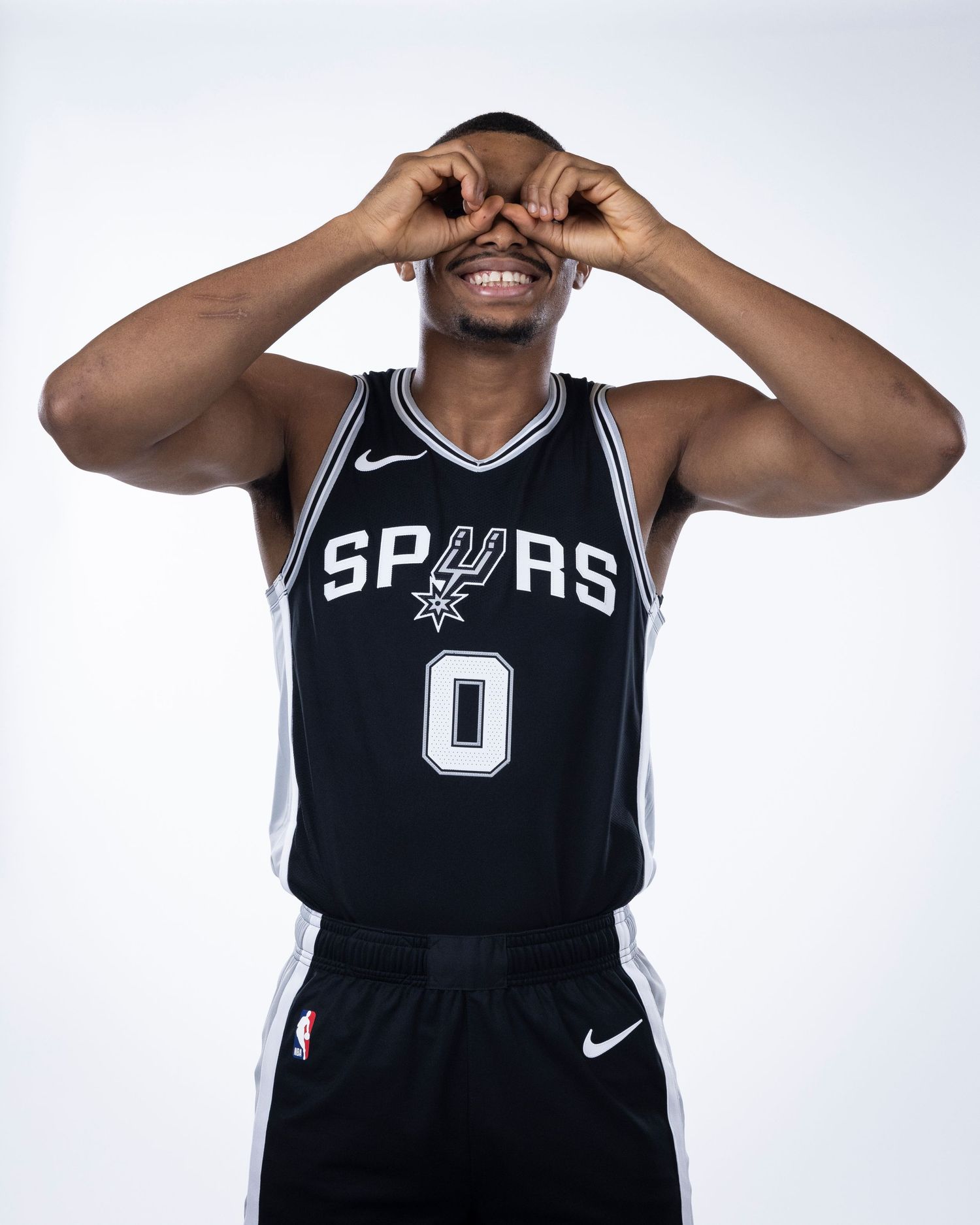 Basketball player in Spurs jersey makes playful gesture during team photo day.
