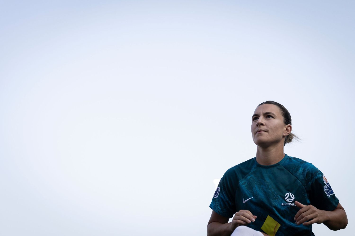 Soccer player in dark jersey looking up against overcast sky.