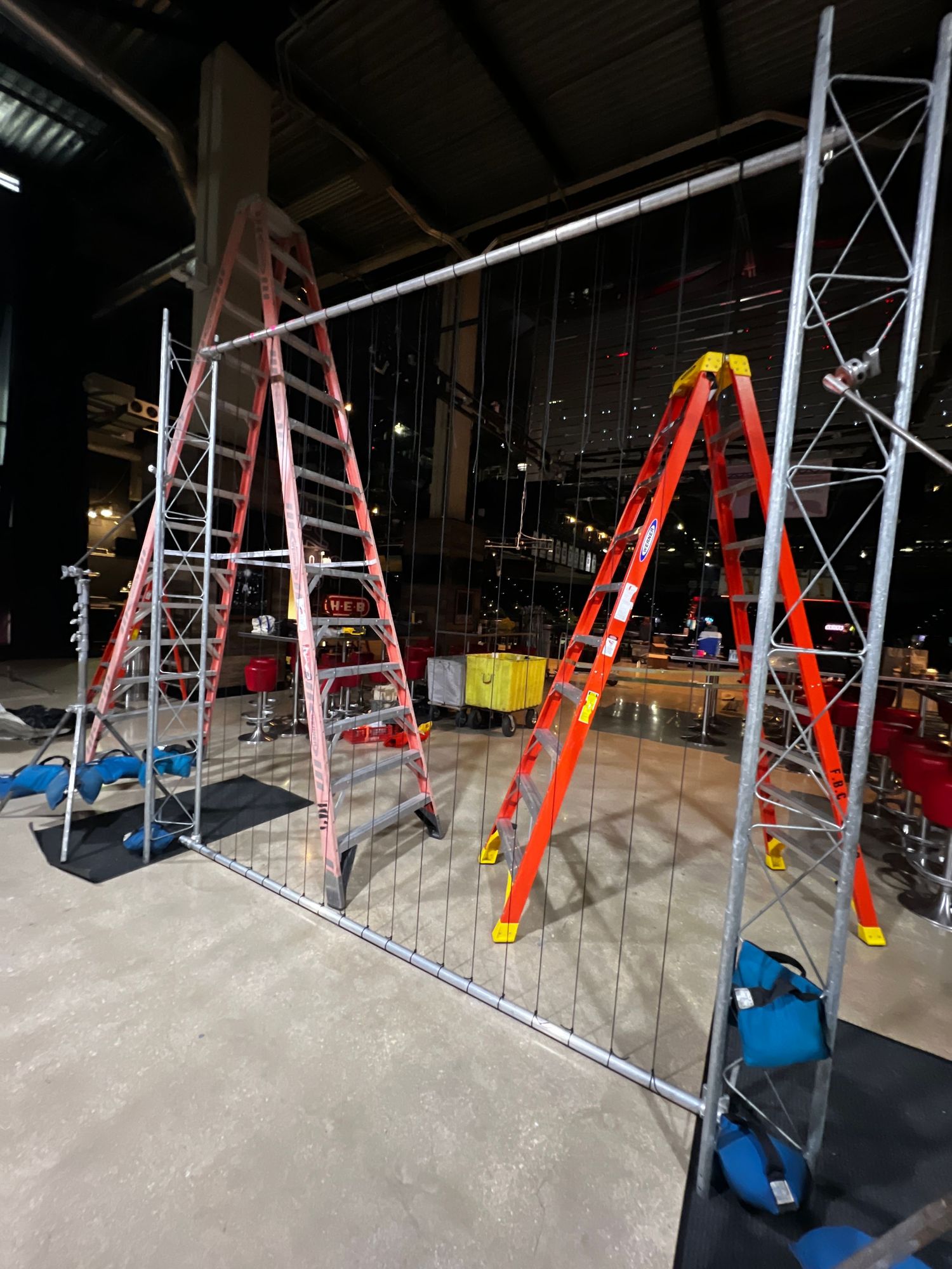 Multiple orange and red ladders lean against scaffolding in a dimly lit construction or renovation area.