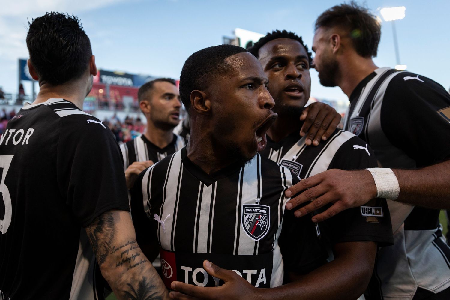 Soccer players in black and white striped jerseys celebrate together during a match.