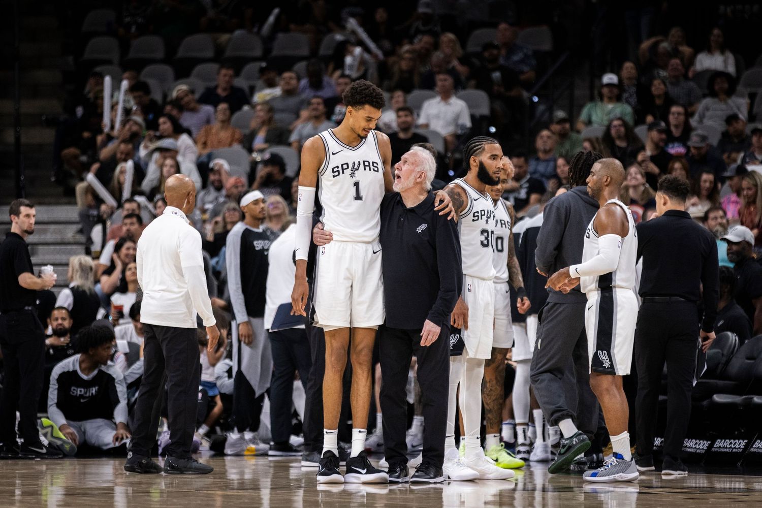 Basketball team and coaching staff gathered during a game break. Gregg Popovich and Victor Wembanyama
