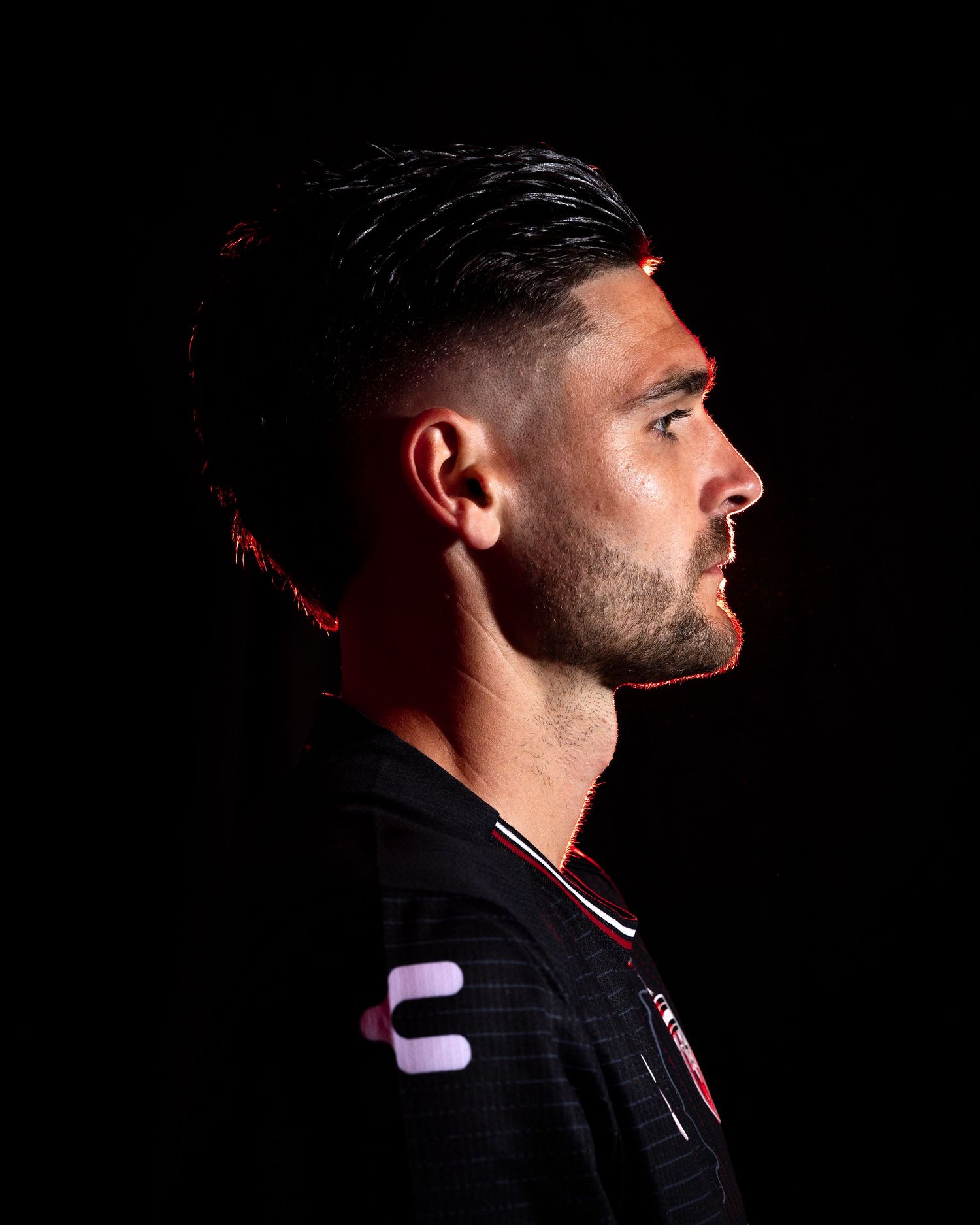 Professional athlete poses in dramatic side profile against dark background wearing black uniform with white trim.