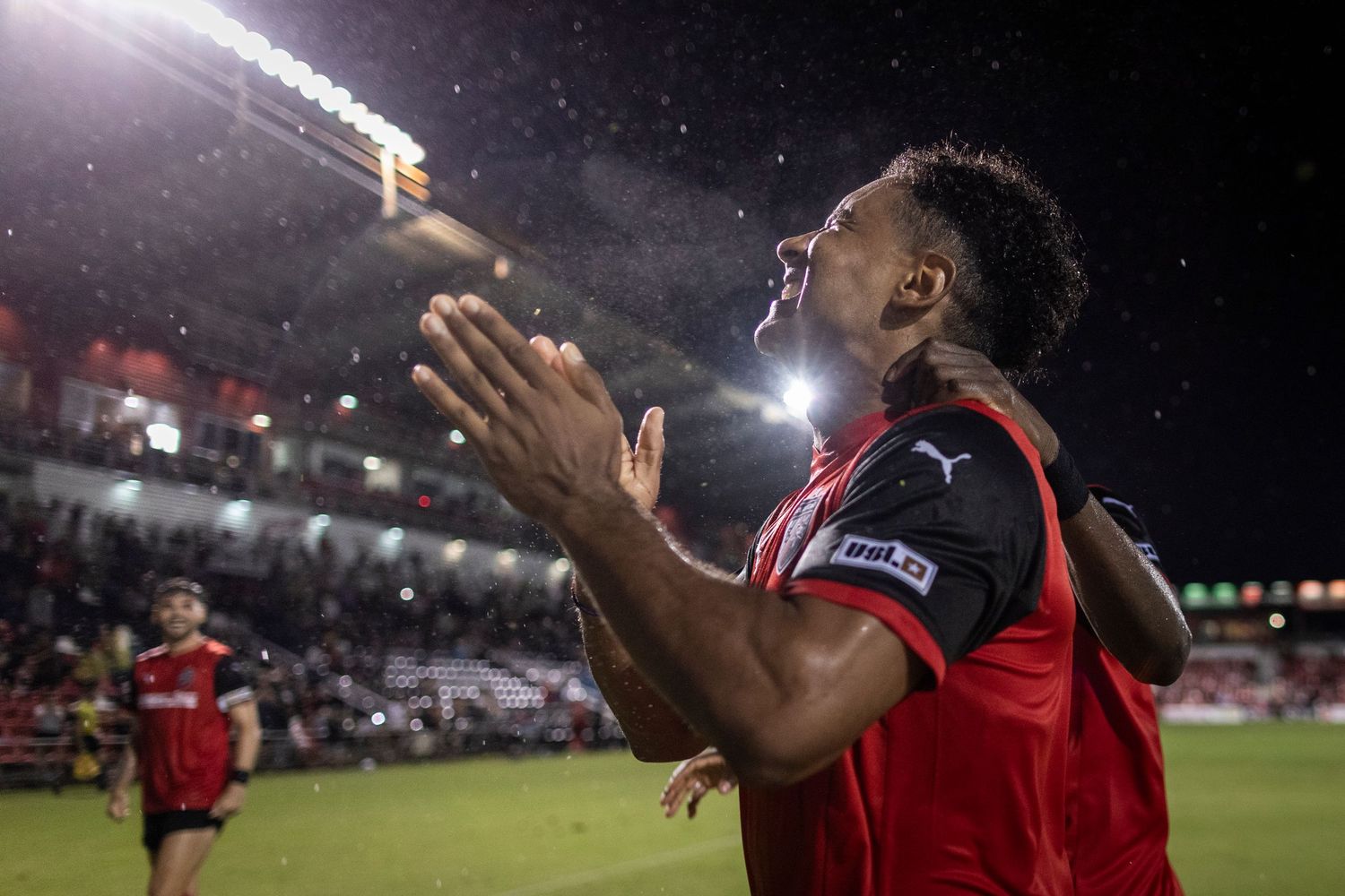 Soccer player celebrates emotionally under stadium lights during nighttime match.