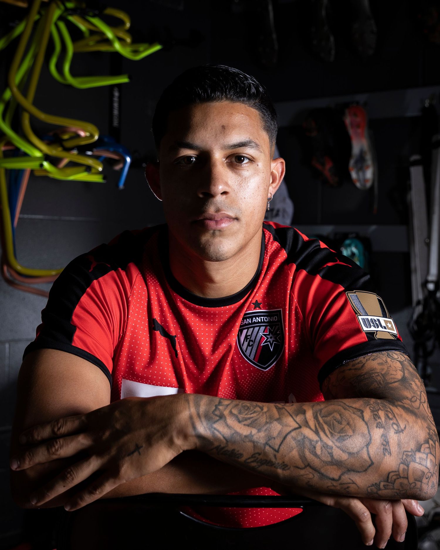 Athletic person in red jersey displays tattooed arms in dramatic lighting.