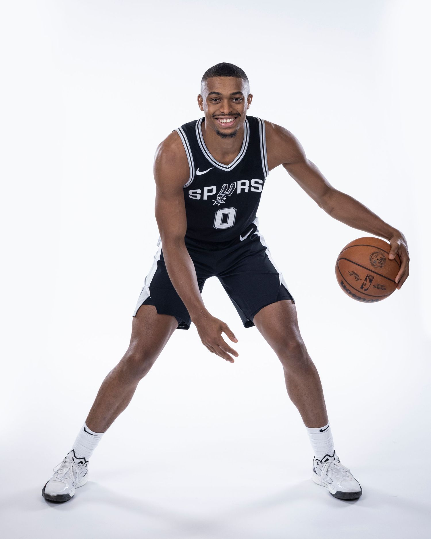 Spurs player in number 0 jersey demonstrates basketball dribbling stance during official team photo session.