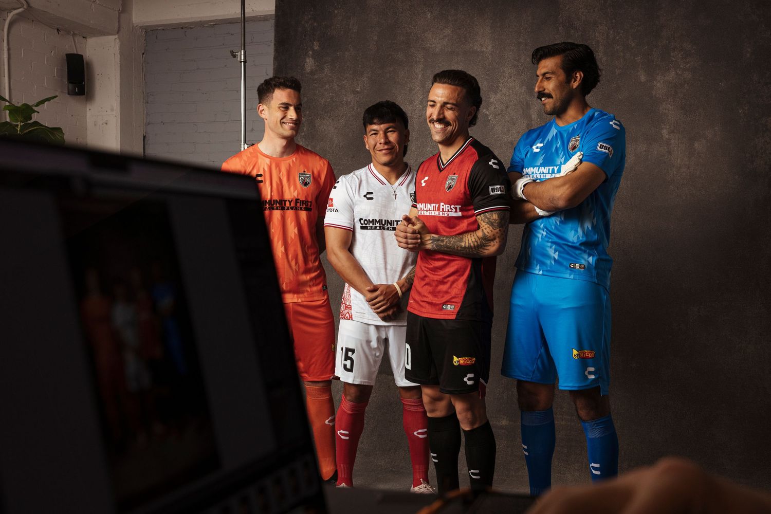 Four soccer players posing in colorful team jerseys during a photo shoot session.