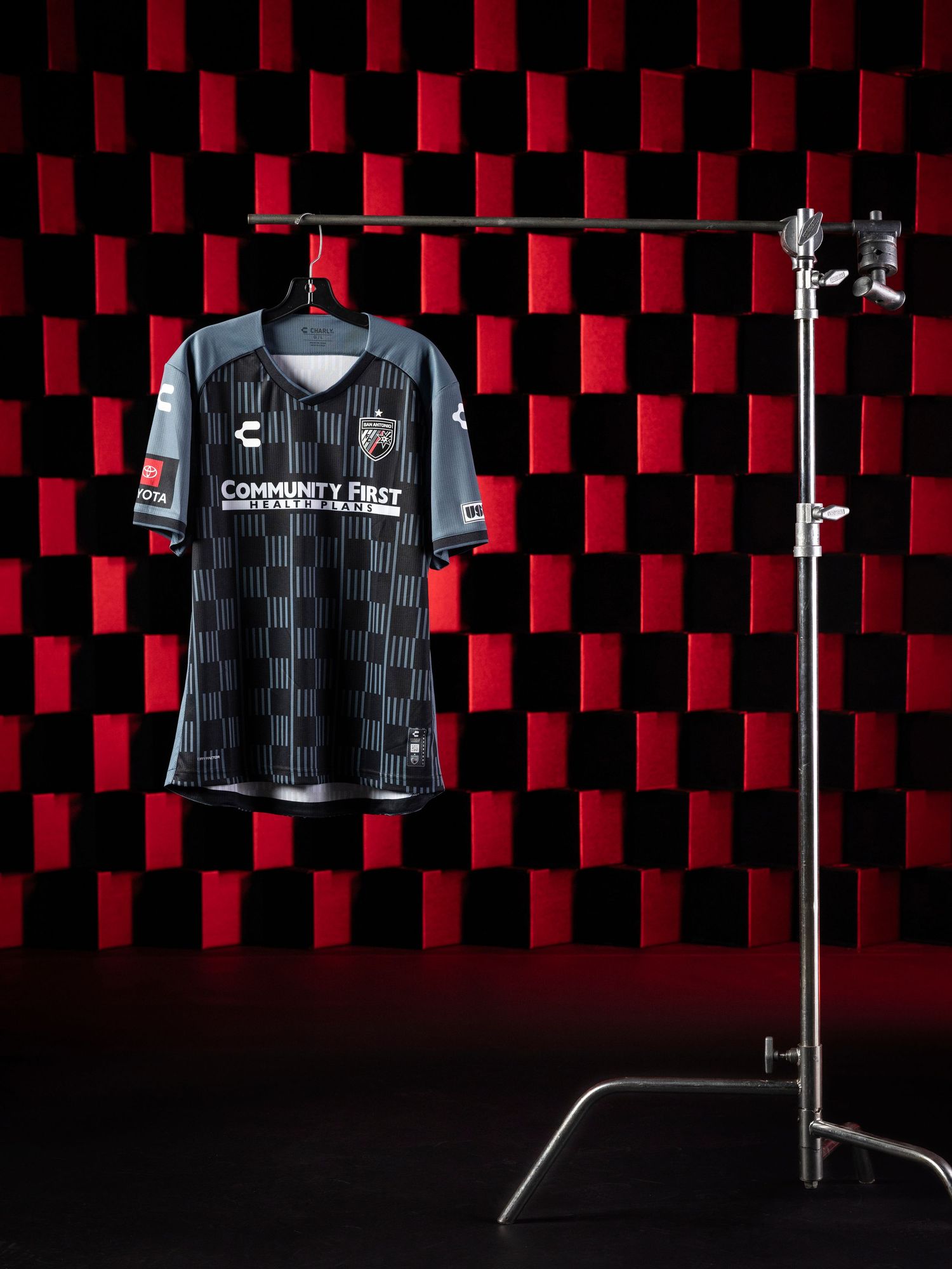 Liverpool FC's 2023-24 away jersey displayed on a black mannequin against a red and black checkered background.