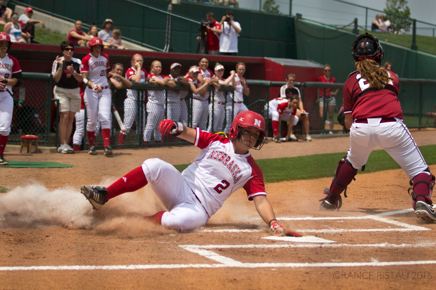 Baseball player sliding into home plate as catcher prepares for play at dusty plate.