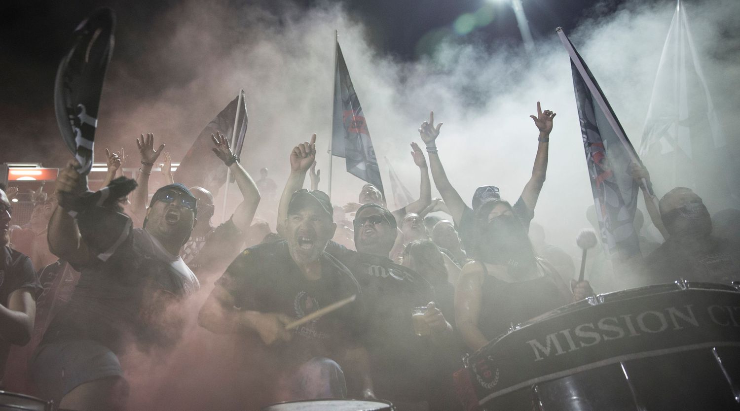 Soccer fans celebrate in a smoky stadium atmosphere waving flags and banners.