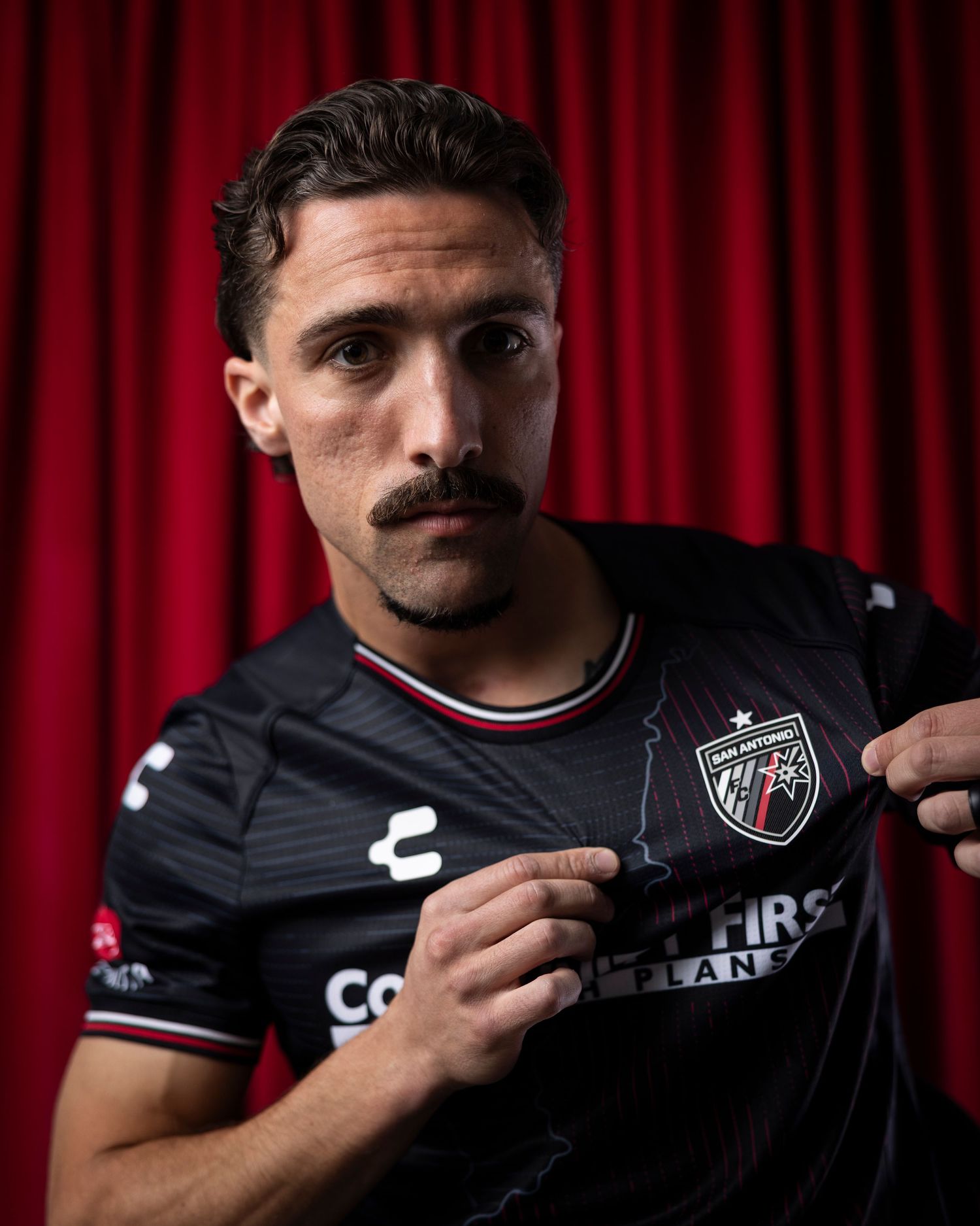 Athlete displays team jersey with Community First sponsorship against red curtain.
