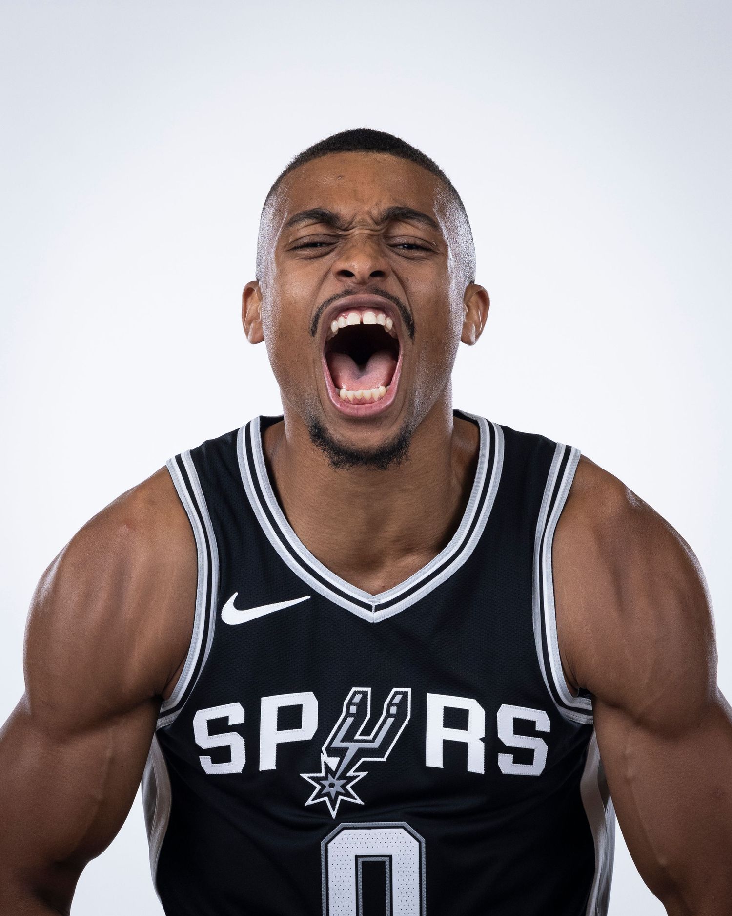 Basketball player in Spurs jersey number 0 shows intense expression during team photoshoot against white background.
