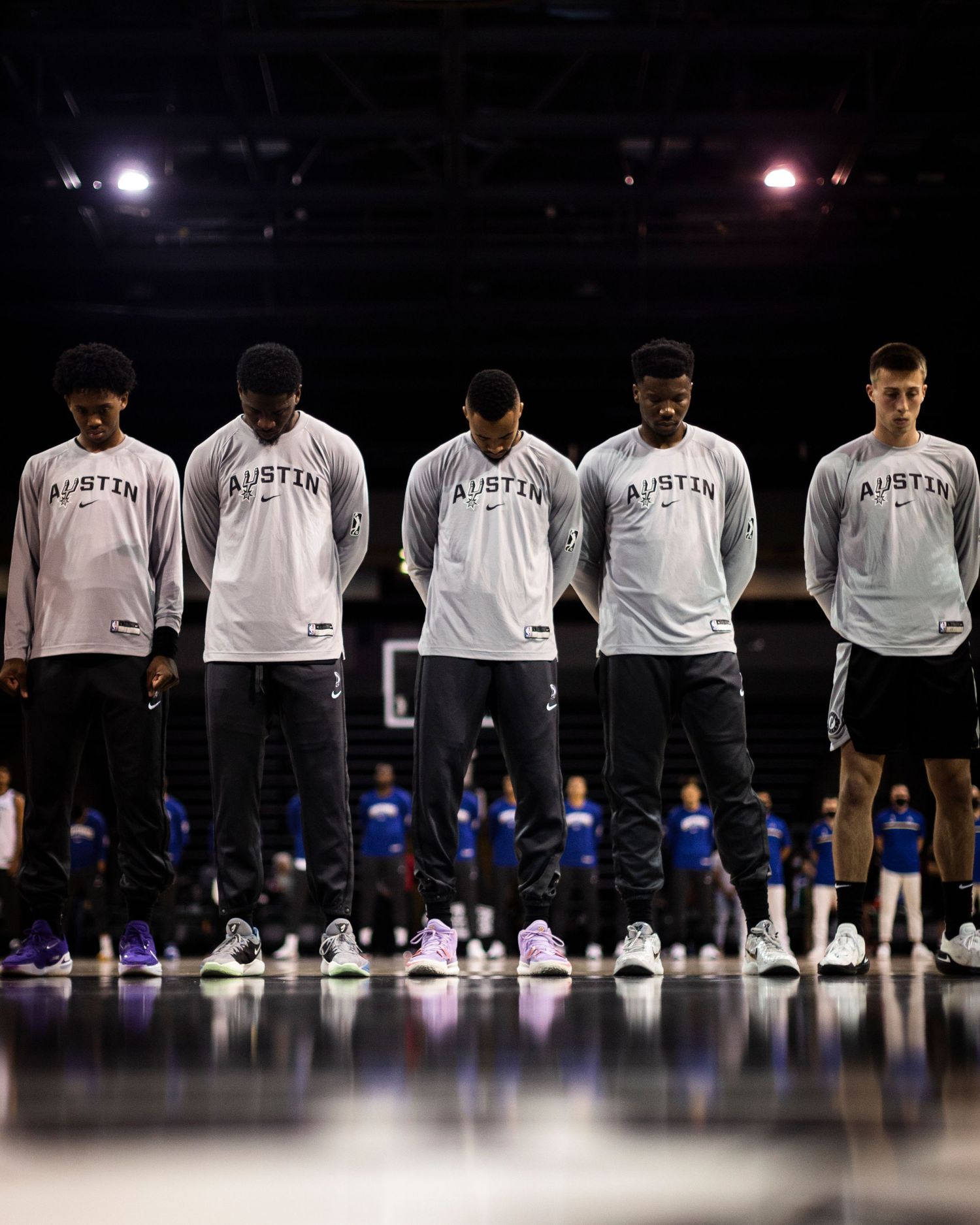 Basketball players lined up in white Austin jerseys before a game on a dark court.