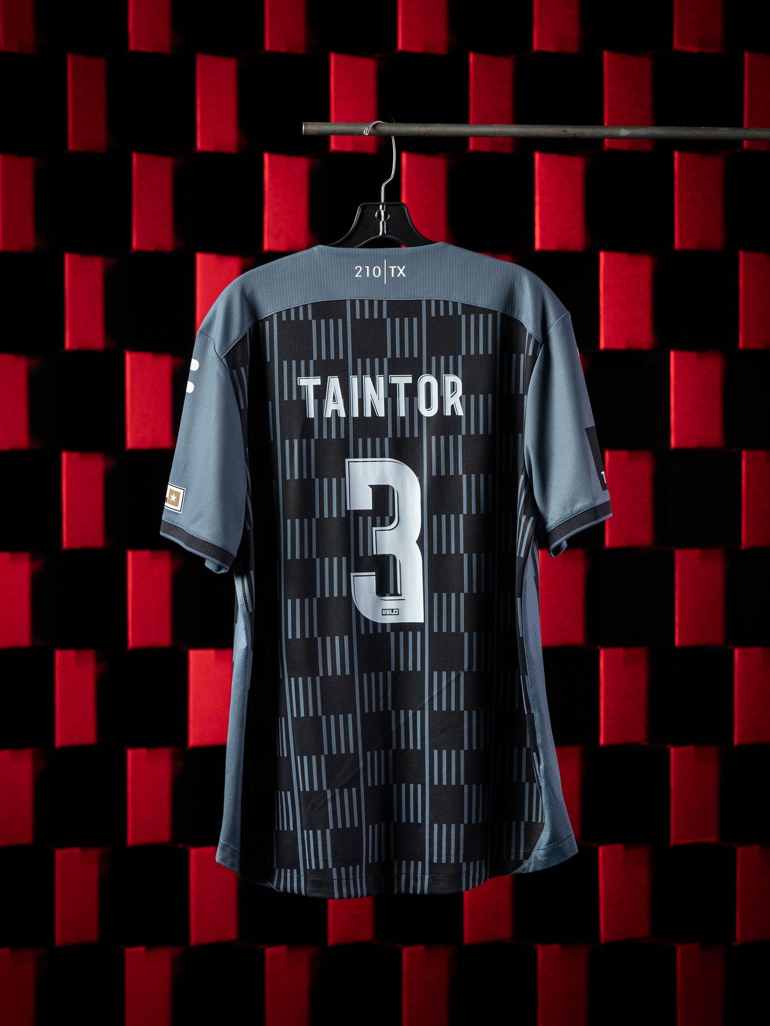 Black soccer jersey with number 3 and name 'TAINTOR' displayed against a red and black checkered background pattern.