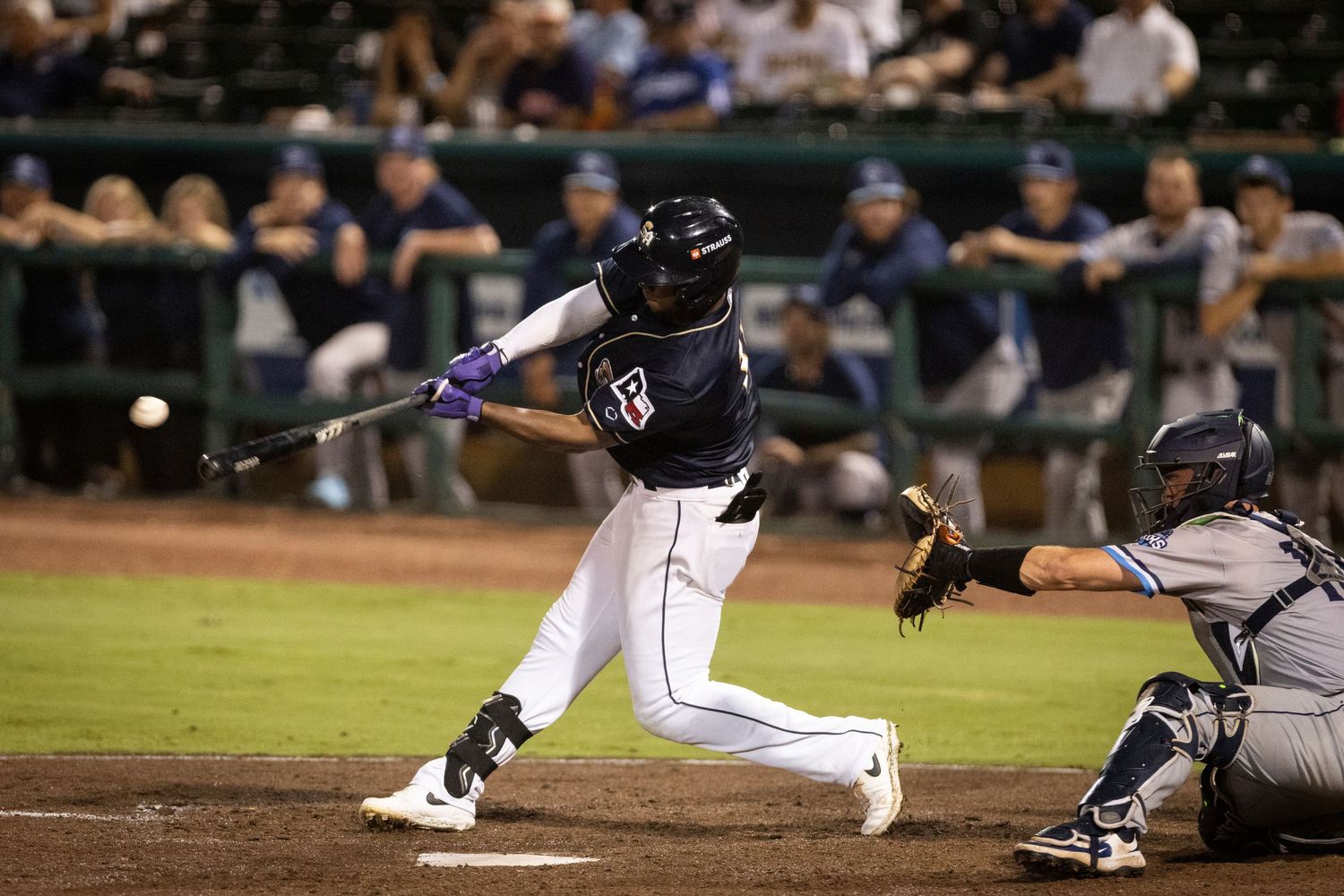 Baseball batter swings at a pitch during a nighttime baseball game.