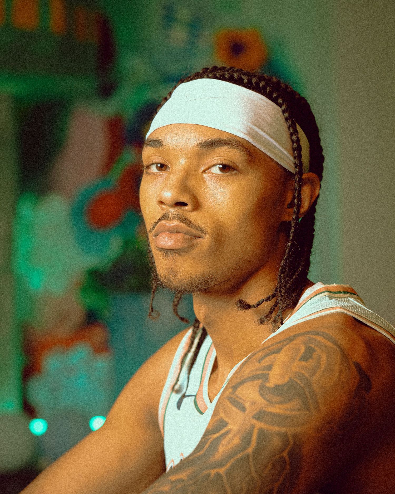 Basketball player in white San Antonio tank poses with headband and tattoos.