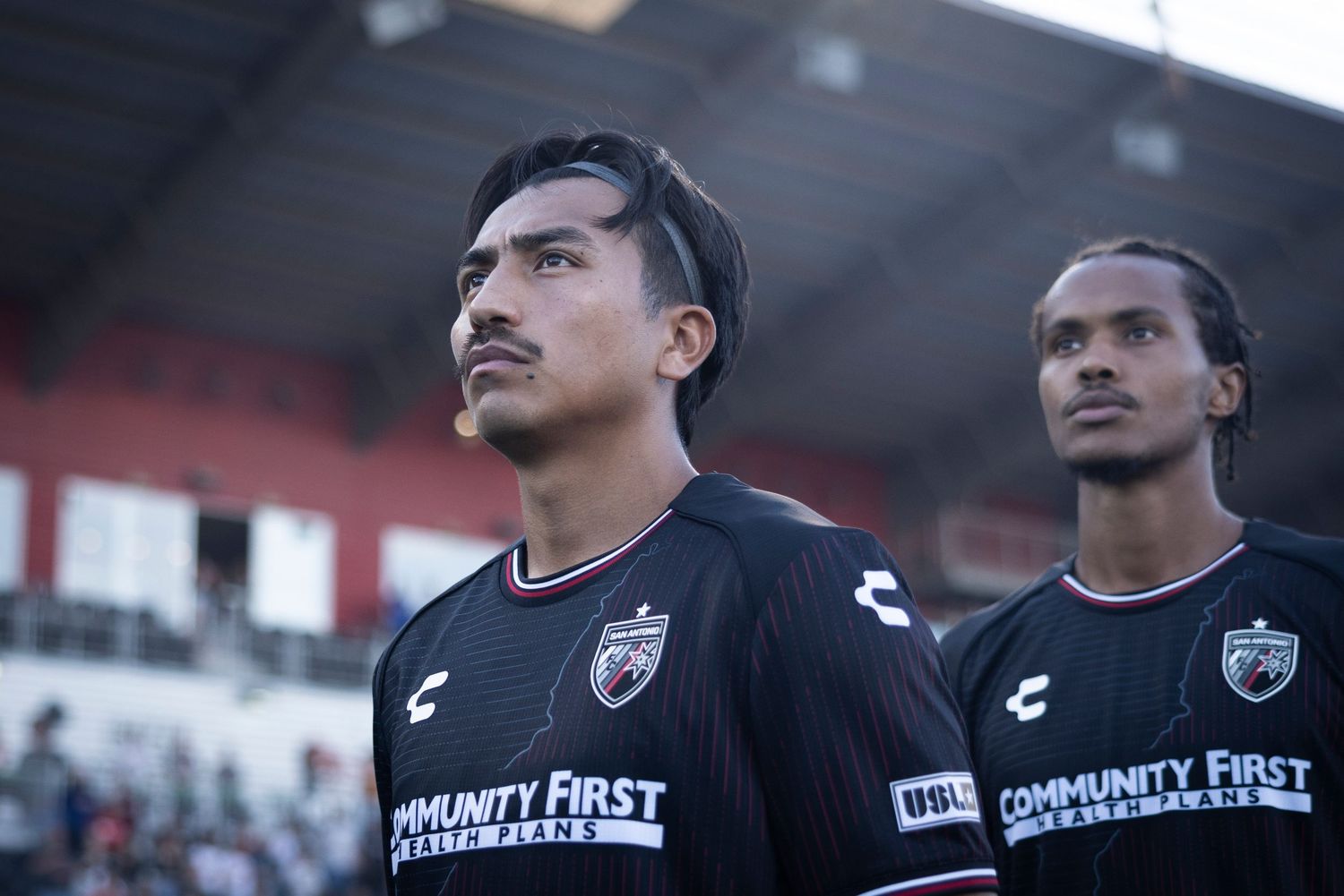 Two soccer players in black uniforms stand ready before a match.