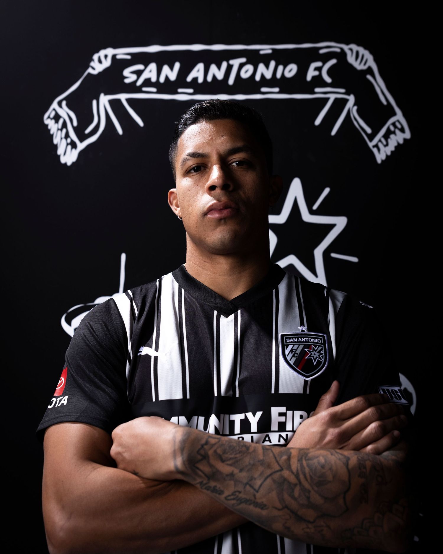 Soccer player in San Antonio FC jersey with neon scarf artwork in background.