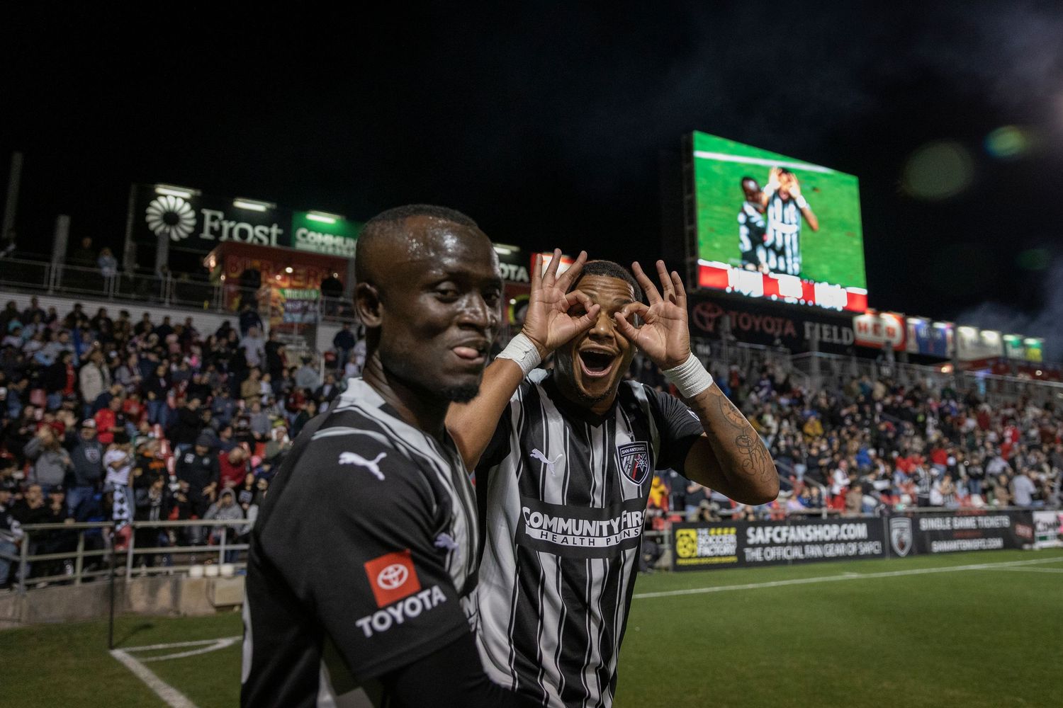 Soccer players in striped referee uniforms make binocular gesture during night game.
