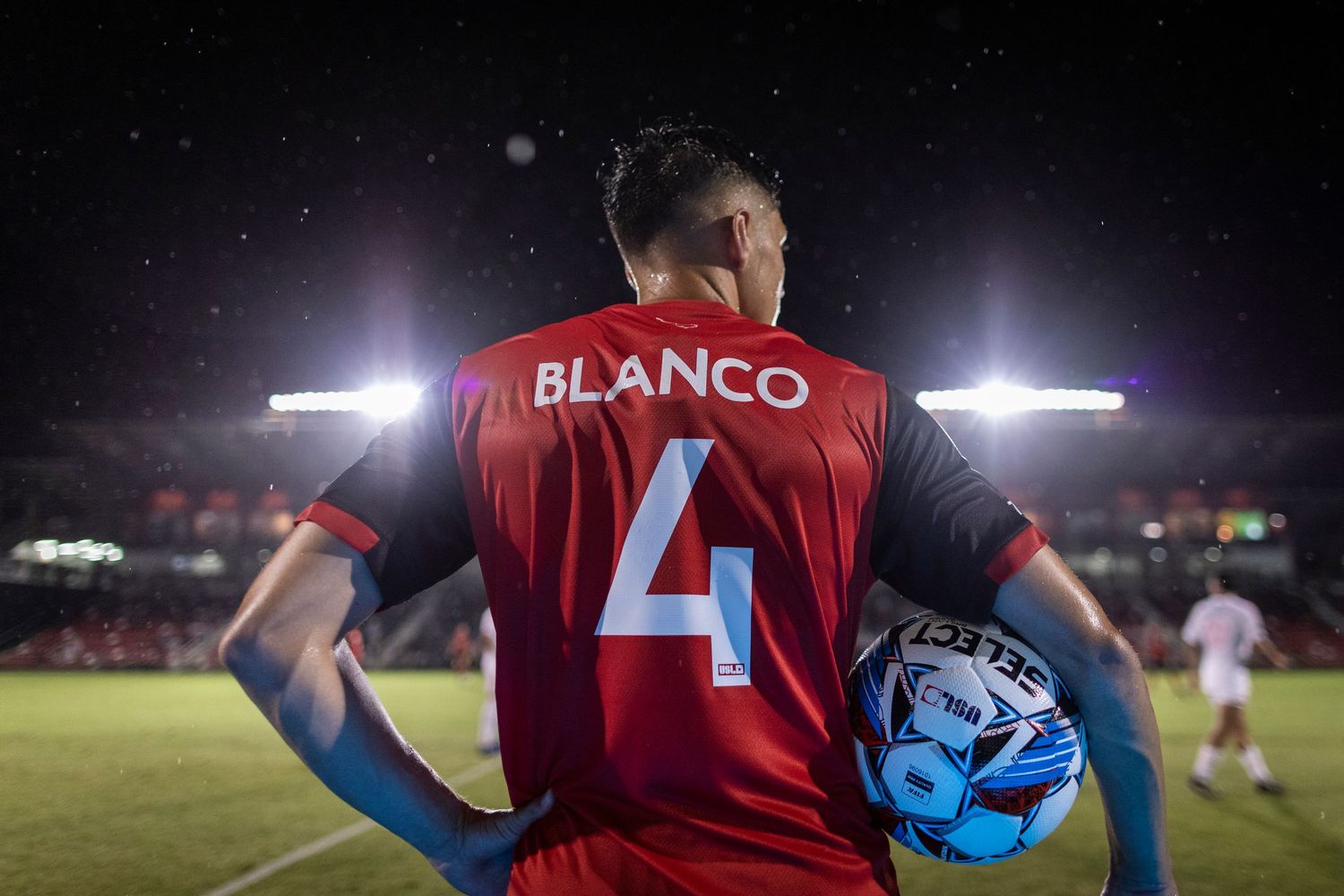 Soccer player wearing red jersey number 4 holds ball during night game.