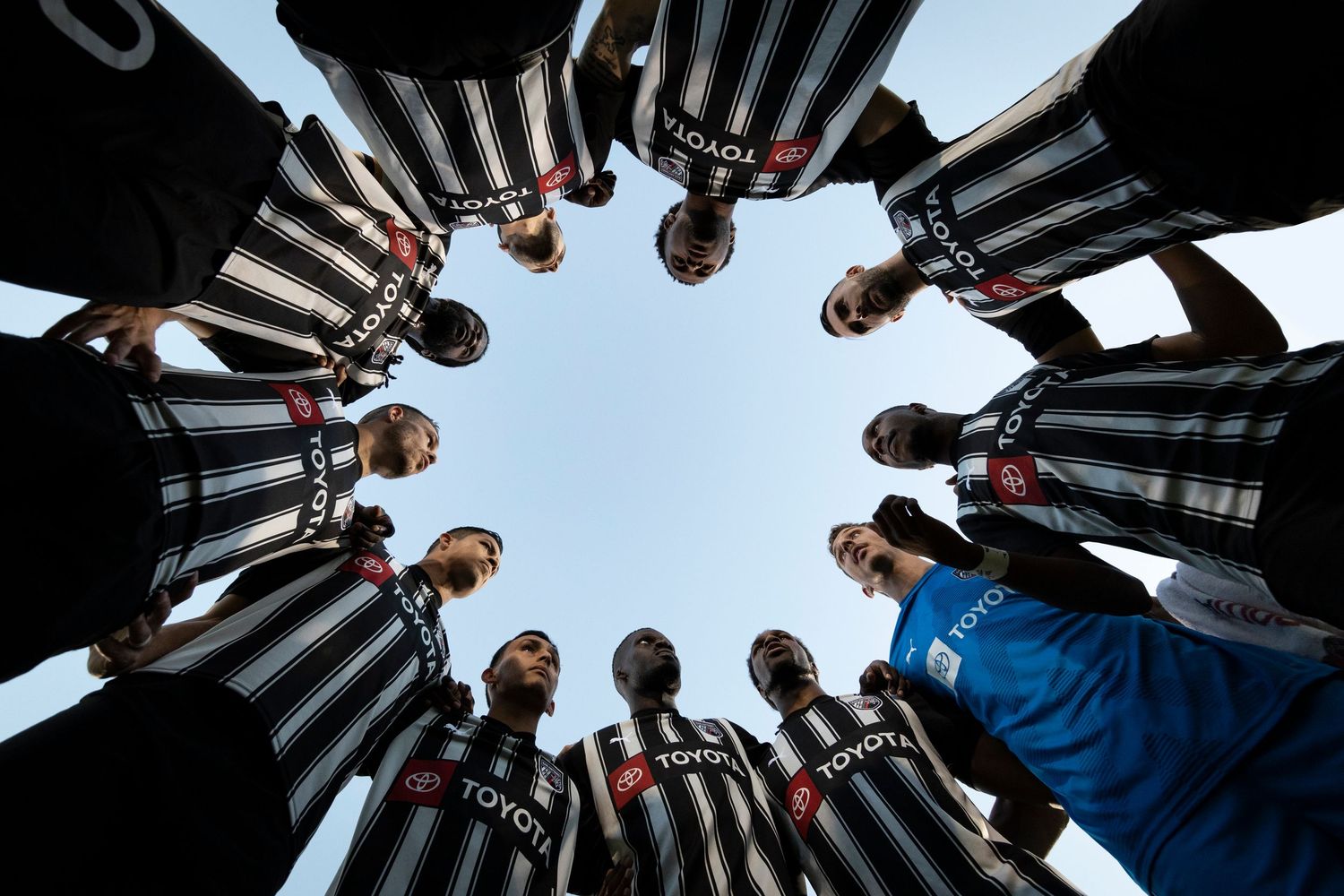 Soccer team huddles in circle formation shot from below against blue sky.