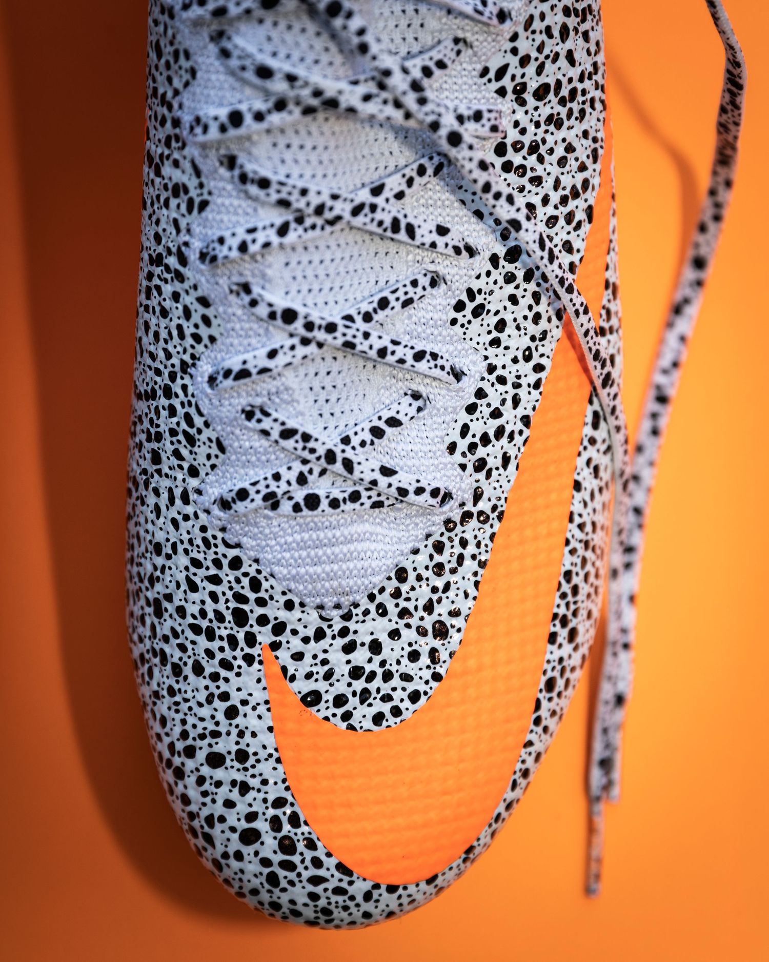 Close-up details of safari print soccer cleats against orange backdrop.