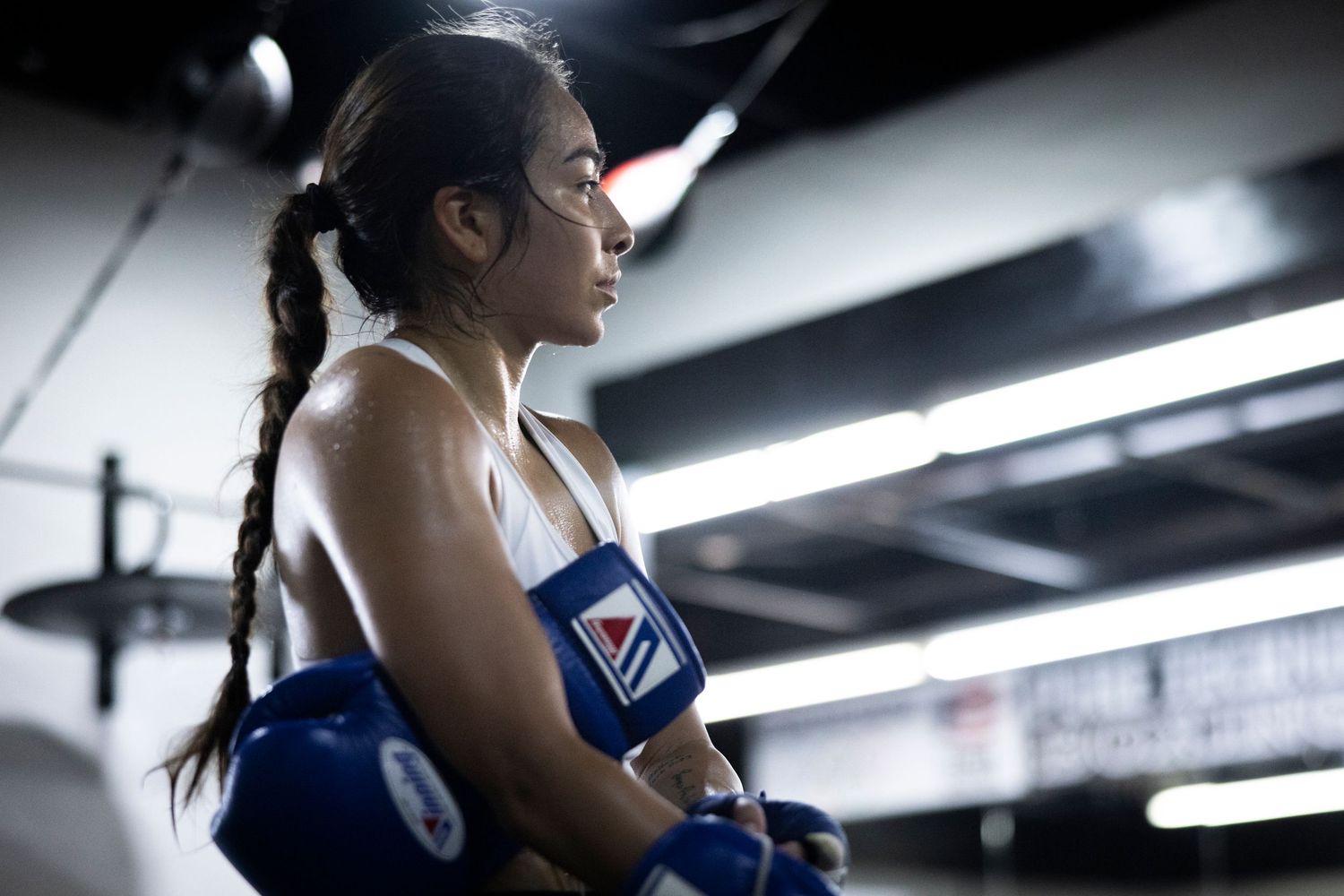 Fighter wearing boxing gloves takes break during training session in dimly lit gym.