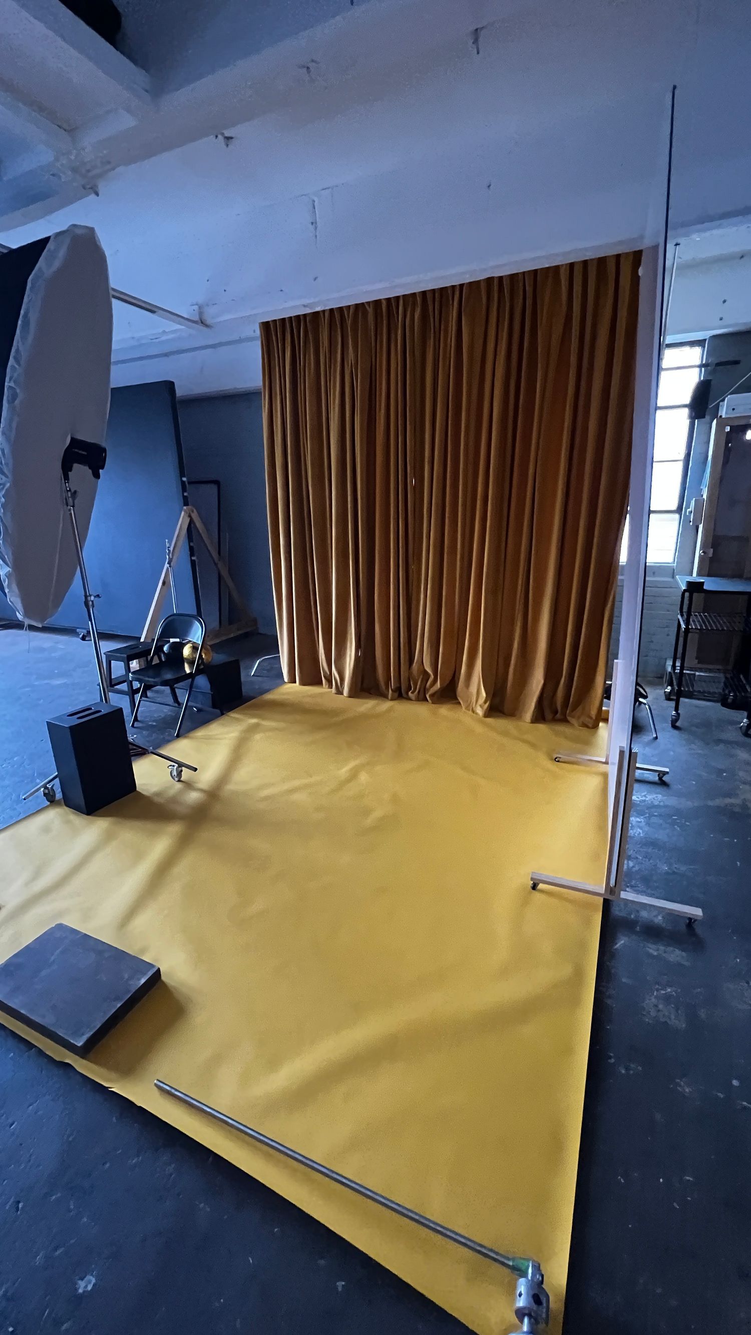 Photography studio setup with yellow backdrop and lighting equipment arranged in a professional indoor space.