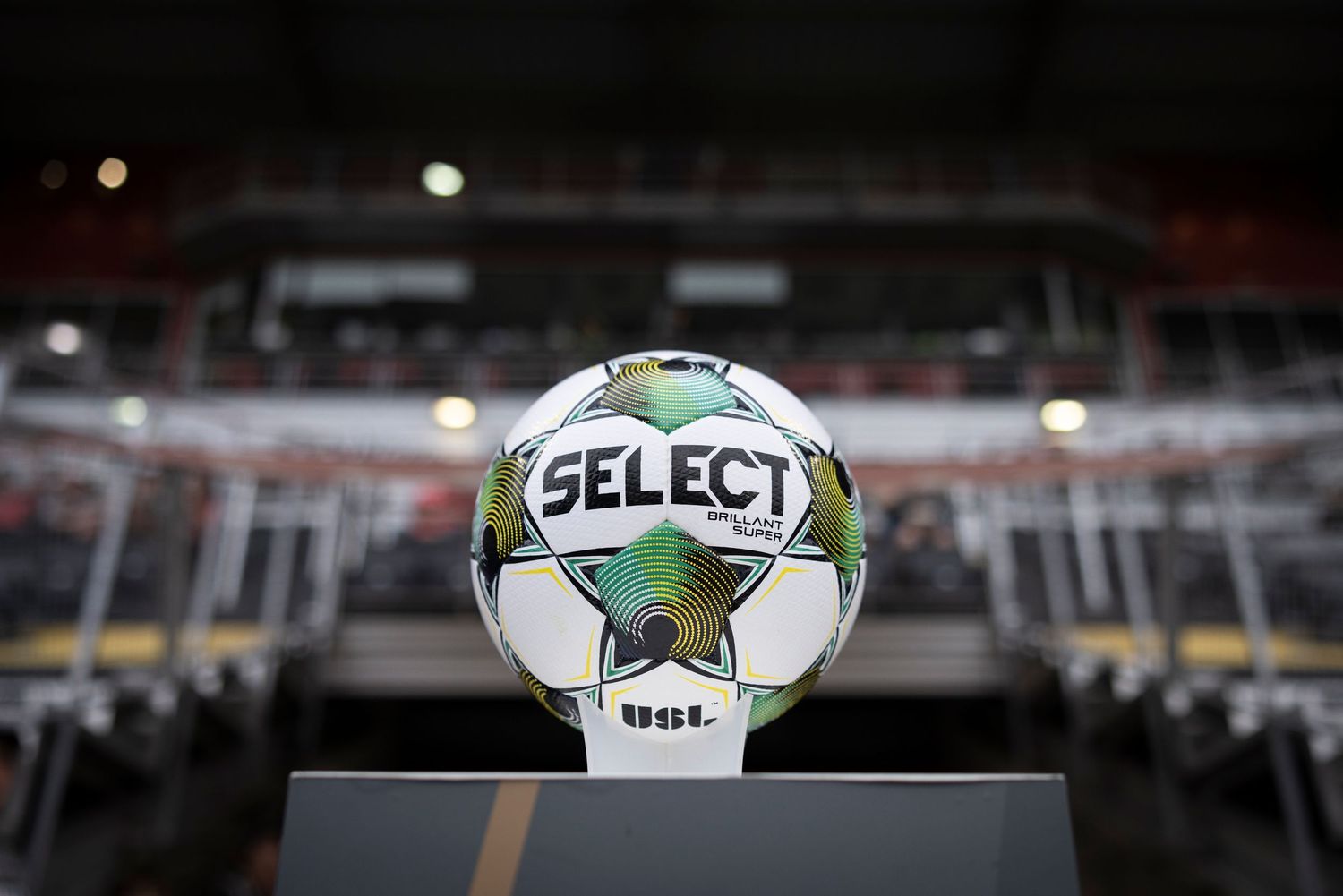 Select brand soccer ball displayed on stand in stadium setting before match.
