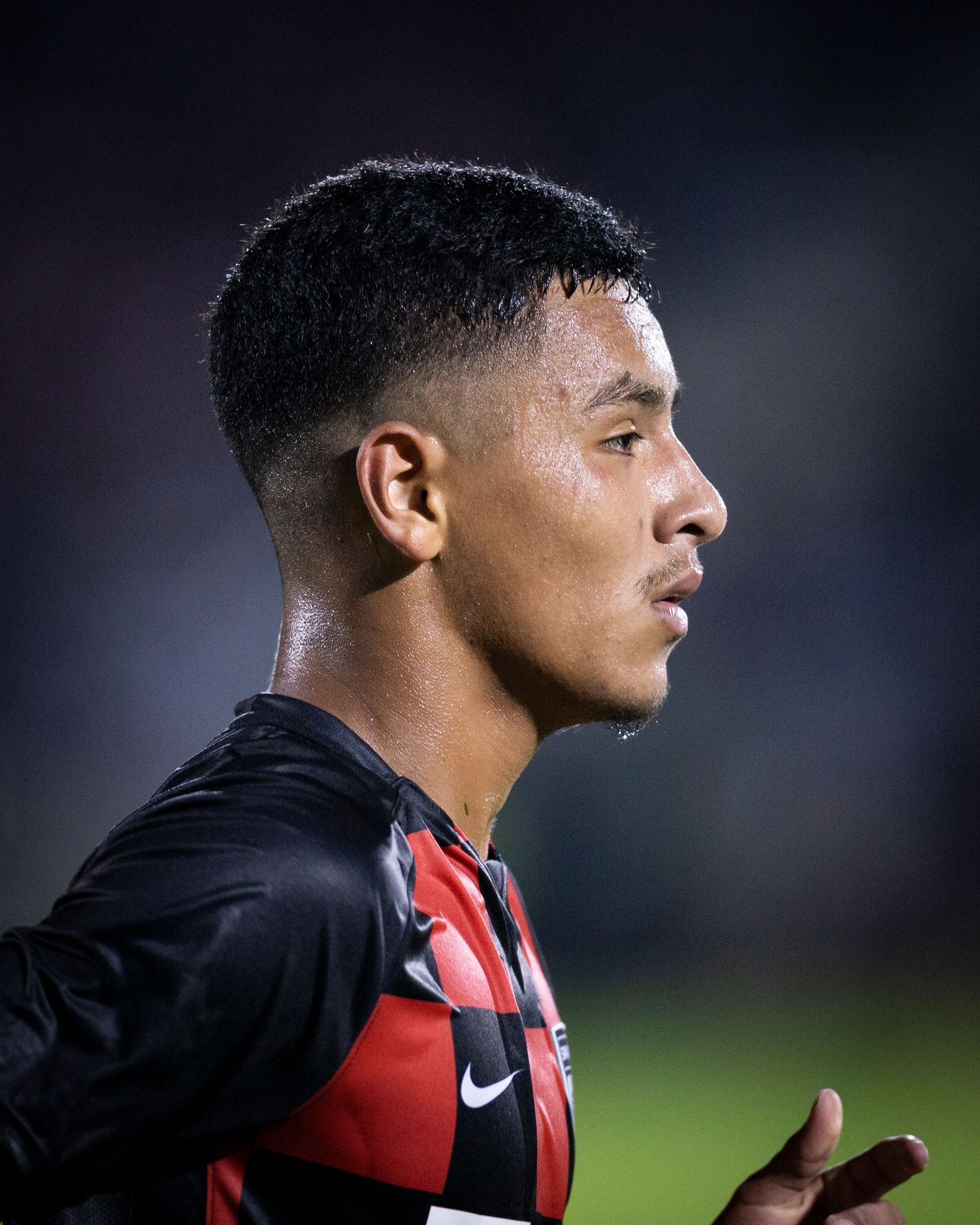 Professional soccer player in black and red jersey shown in side profile against dark background.