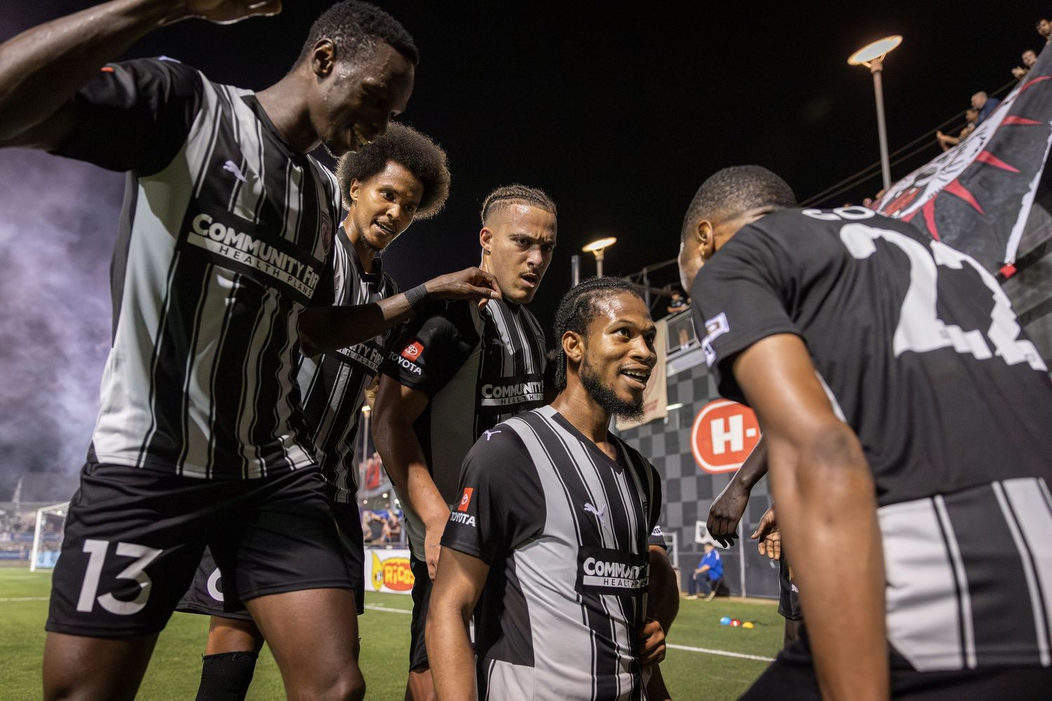 Soccer players gather in a close group discussion during a night match.