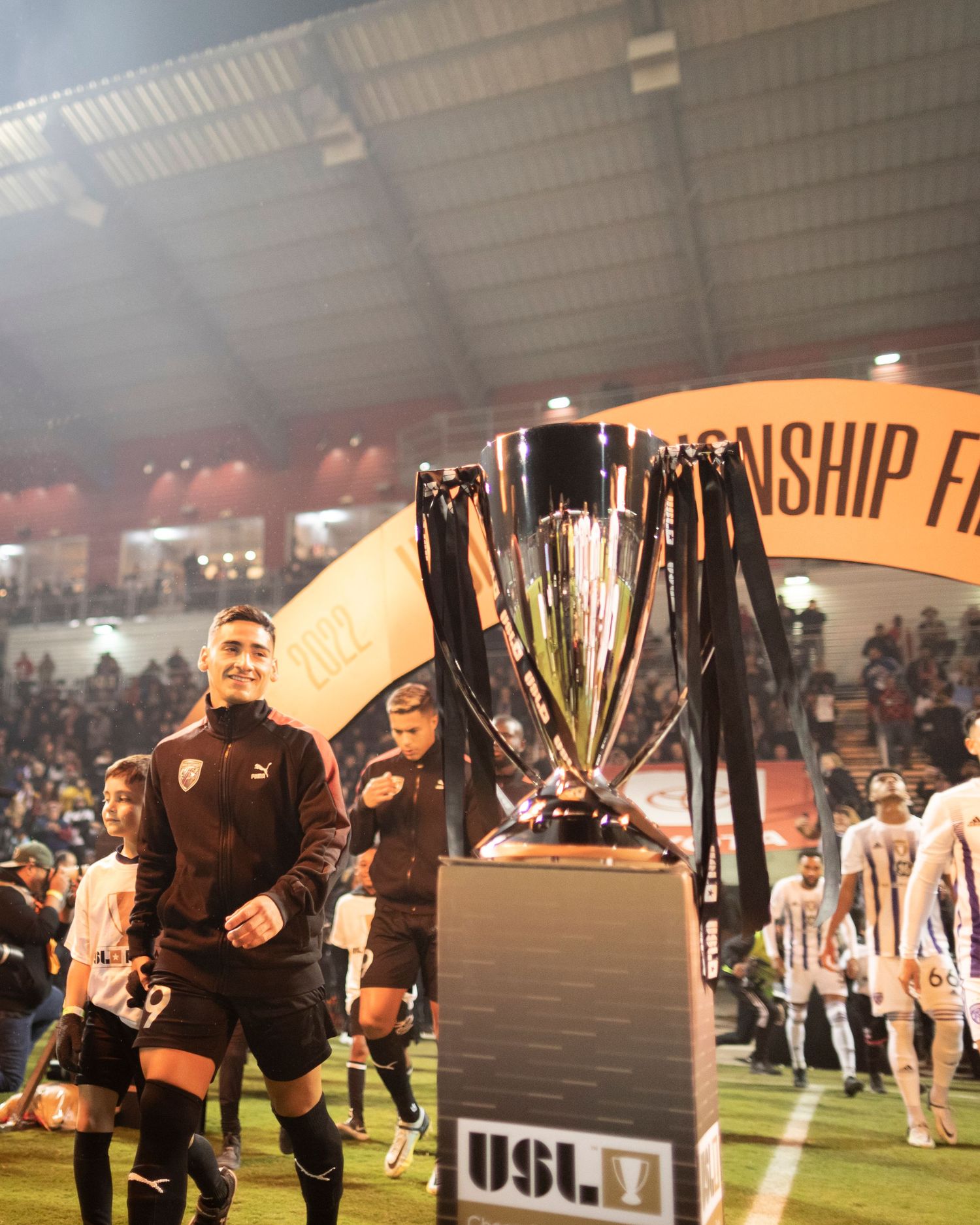USL Championship trophy displayed on field with players in background.