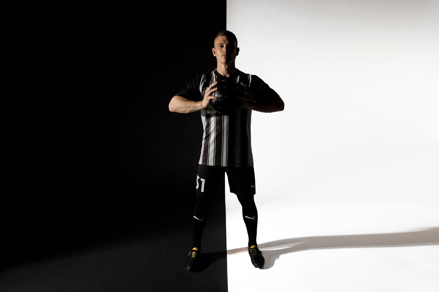 Dramatic silhouette of athlete in black uniform against white backdrop.