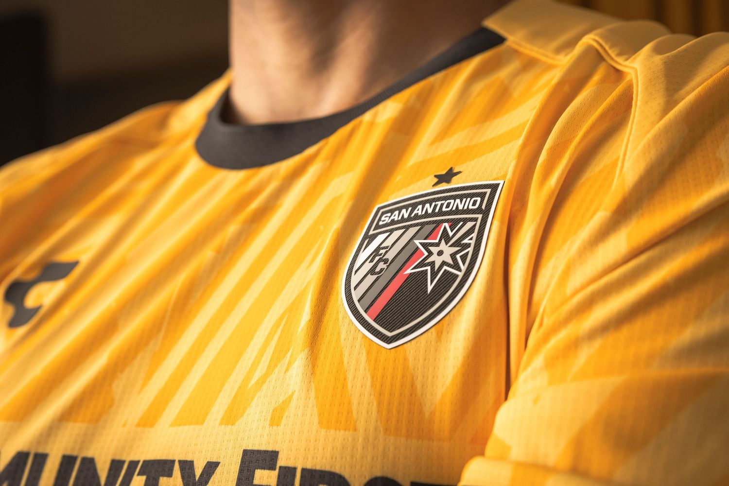 Yellow soccer jersey displaying team crest and sponsor logo against dark background.