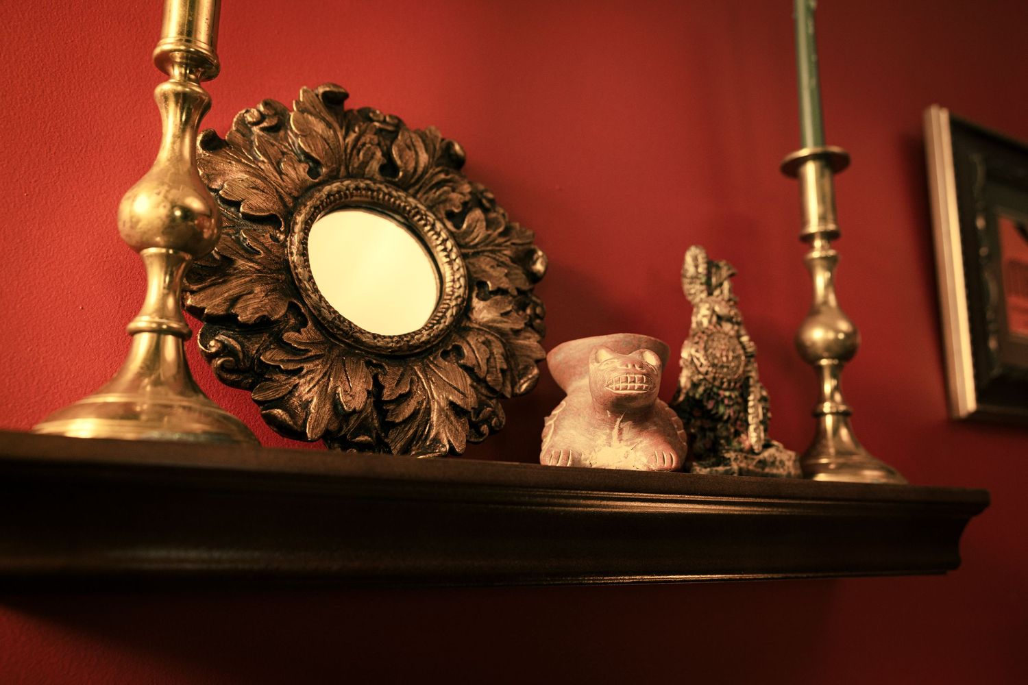 Ornate gold candlesticks and decorative mirrors create an elegant display against a deep red wall in warm lighting.