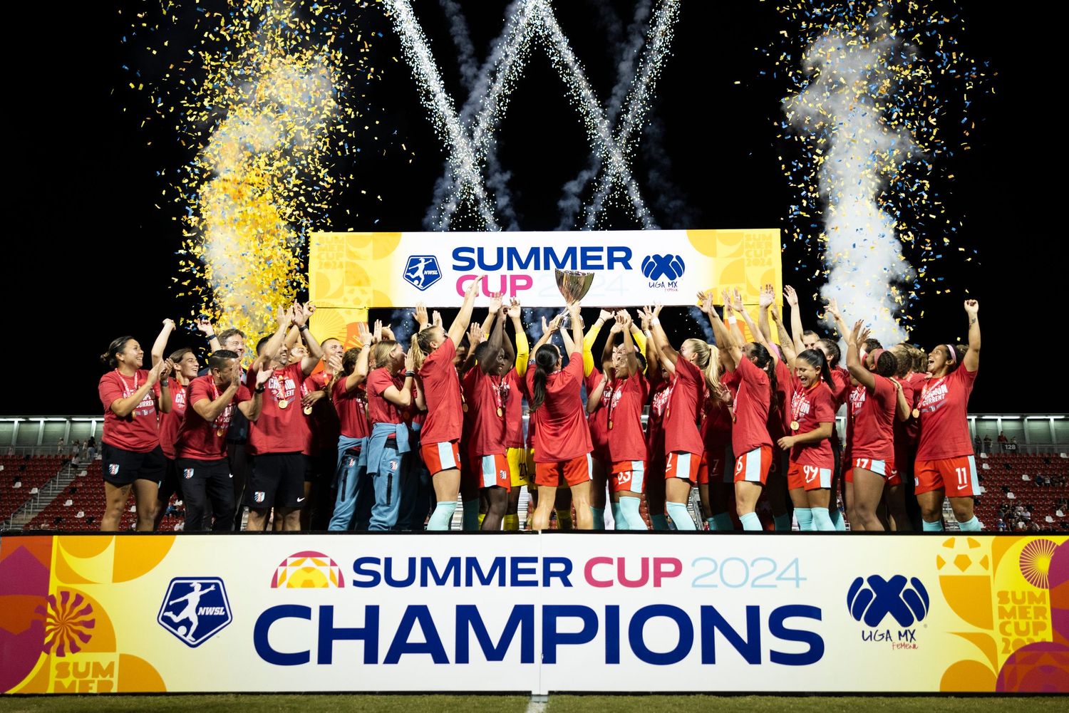 Championship celebration with confetti as team lifts Summer Cup trophy on stage with banner.
