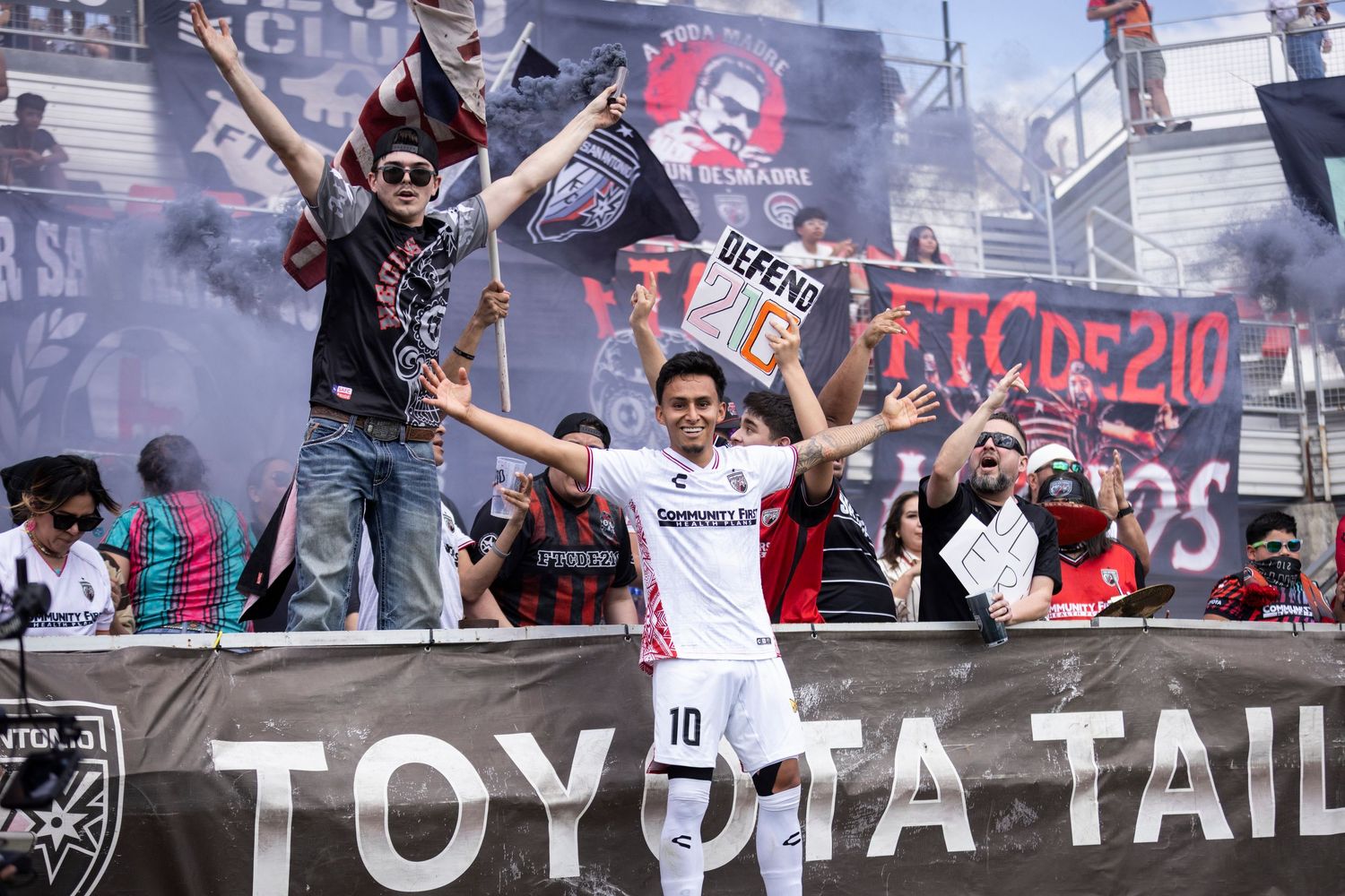 Soccer player in white number 10 jersey celebrates with passionate fan supporters section.