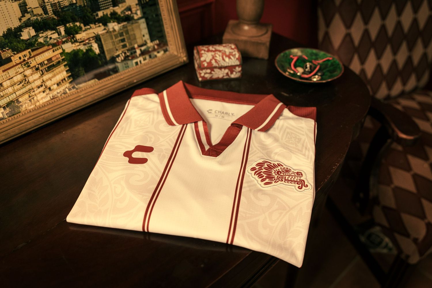 White and red Chivas soccer jersey folded on a dark wooden table with decorative items in the background.
