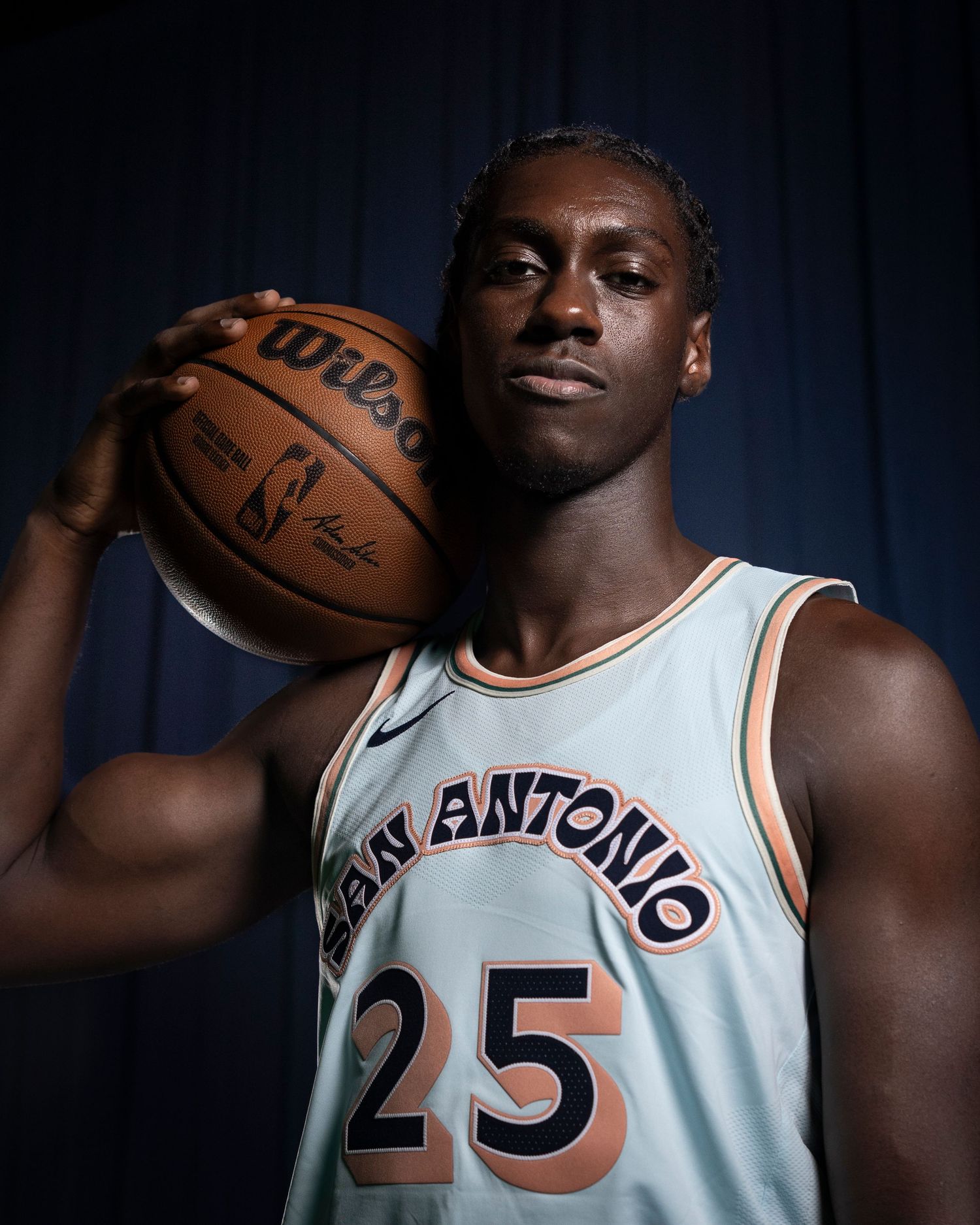 Basketball player in San Antonio jersey 25 poses with ball in dramatic studio lighting.