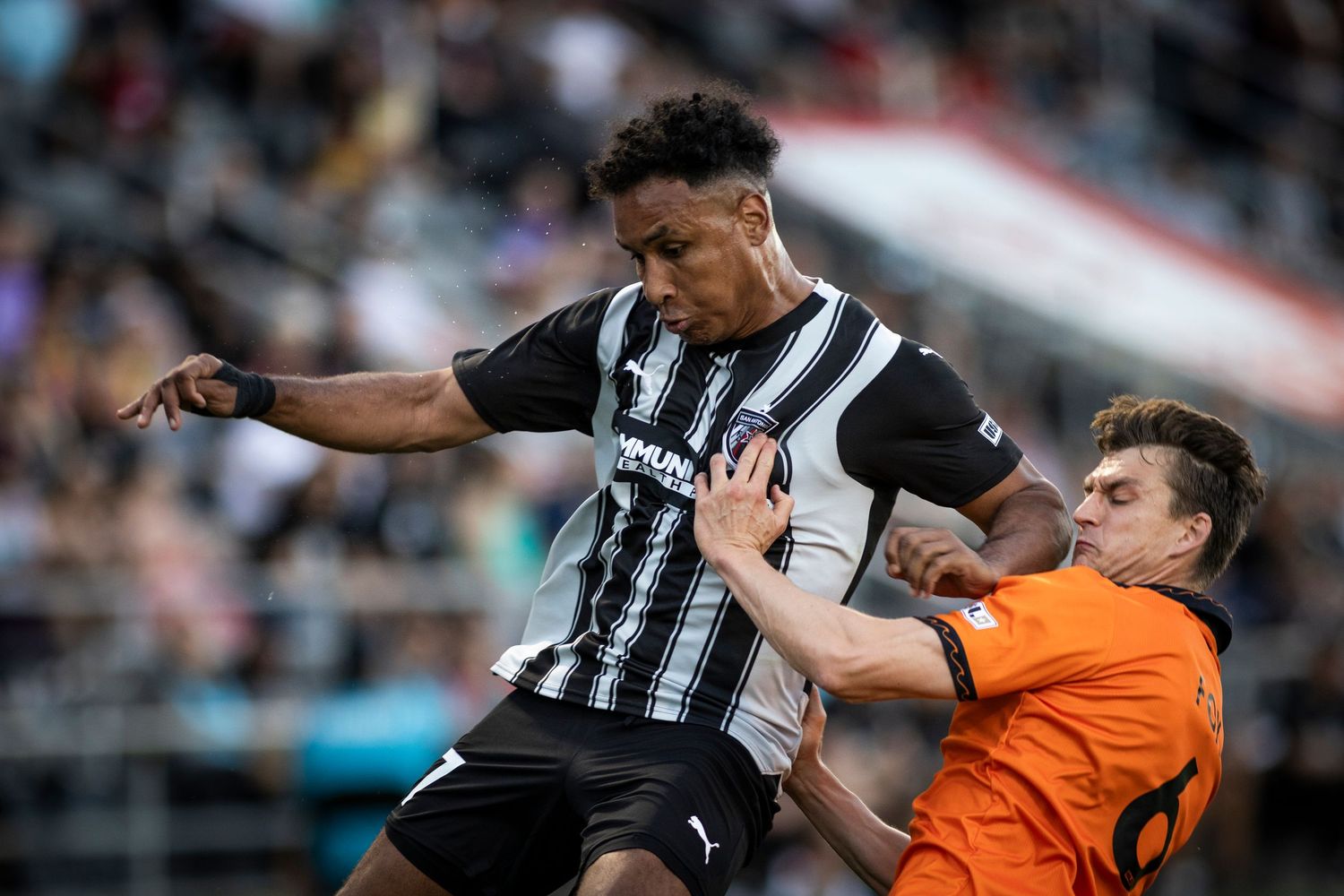 Athletic play between soccer players in striped black jersey and orange uniform during match.