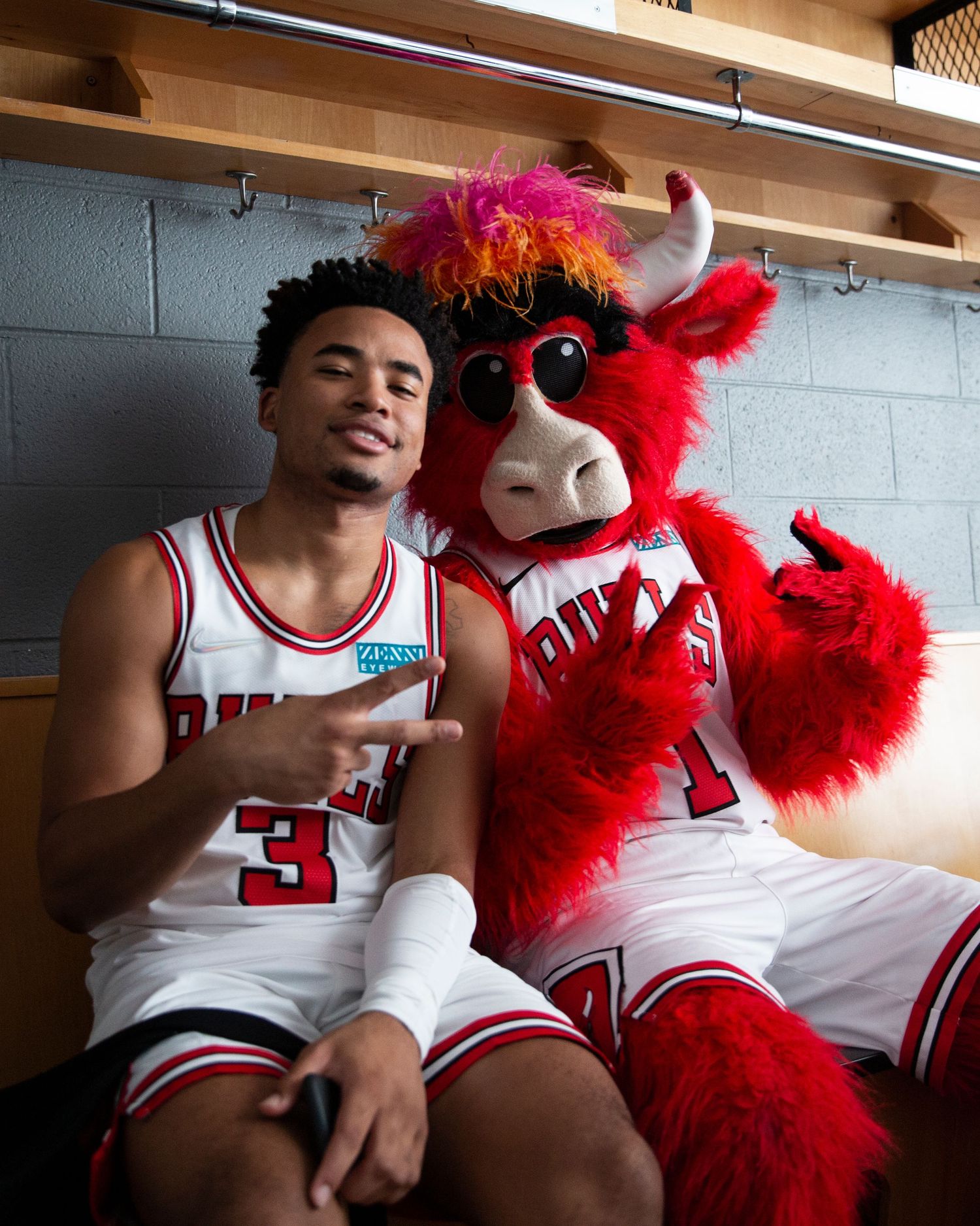 Bulls player and mascot posing together in locker room.